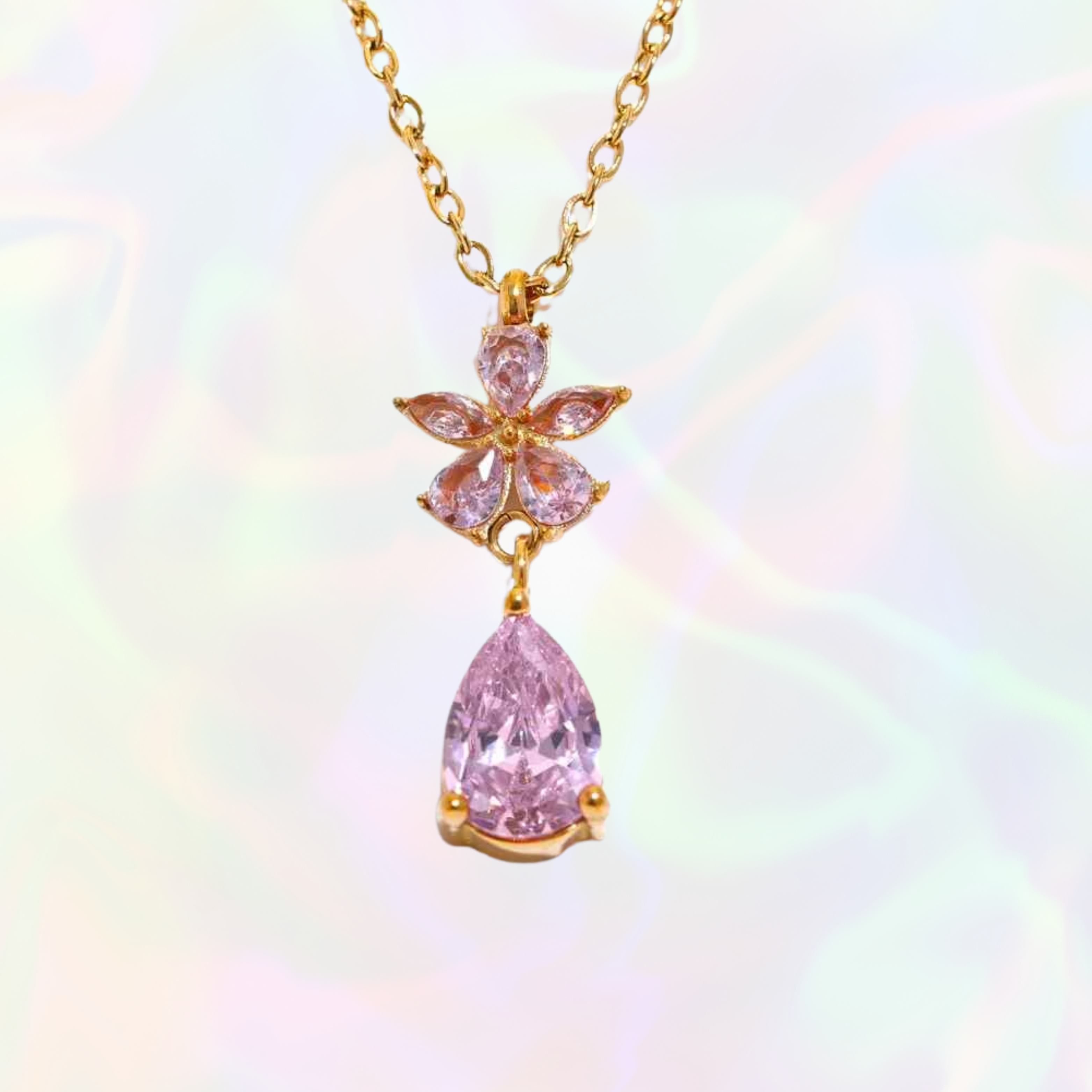 Pink teardrop pendant necklace with gold flower accent on a gold chain against a rainbow gradient background
