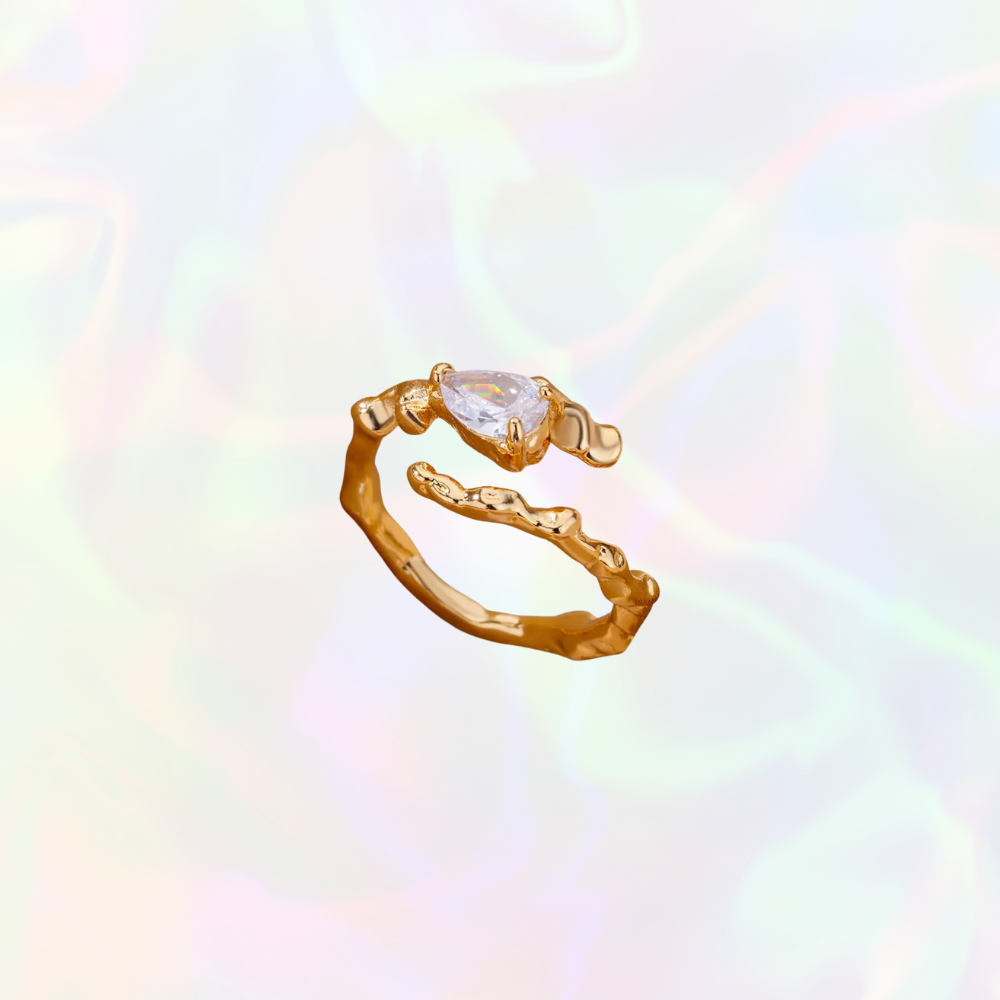 Gold organic shaped ring with a clear gemstone on a multicolored background