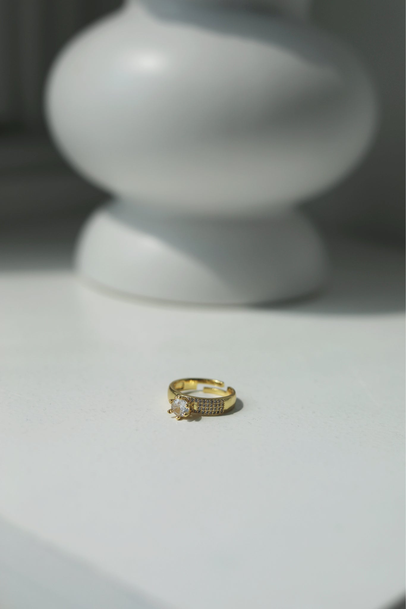 Gold ring with small diamonds on a light surface with a blurred white vase in the background