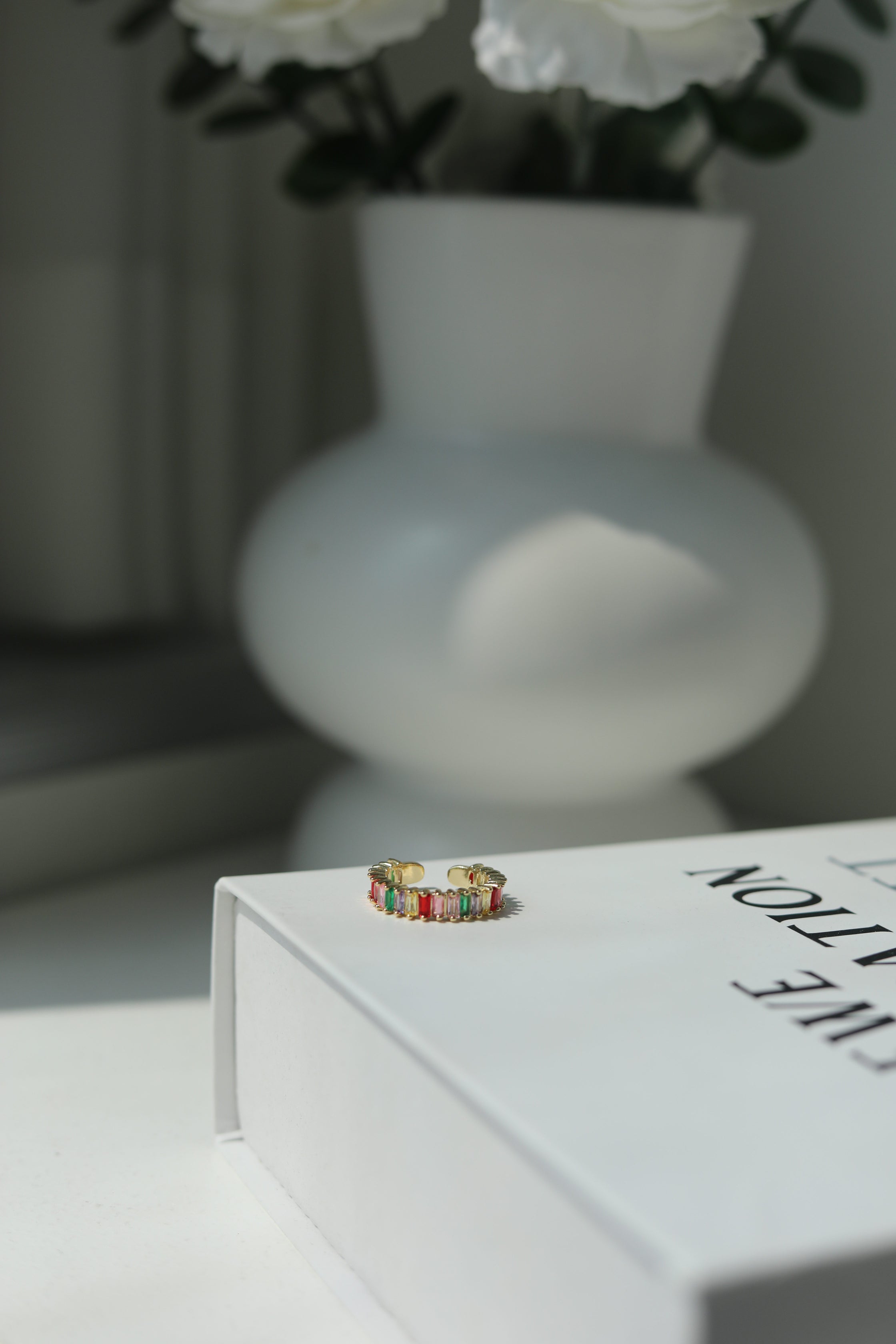 Colorful ring on a white book with a blurred vase and flowers in the background