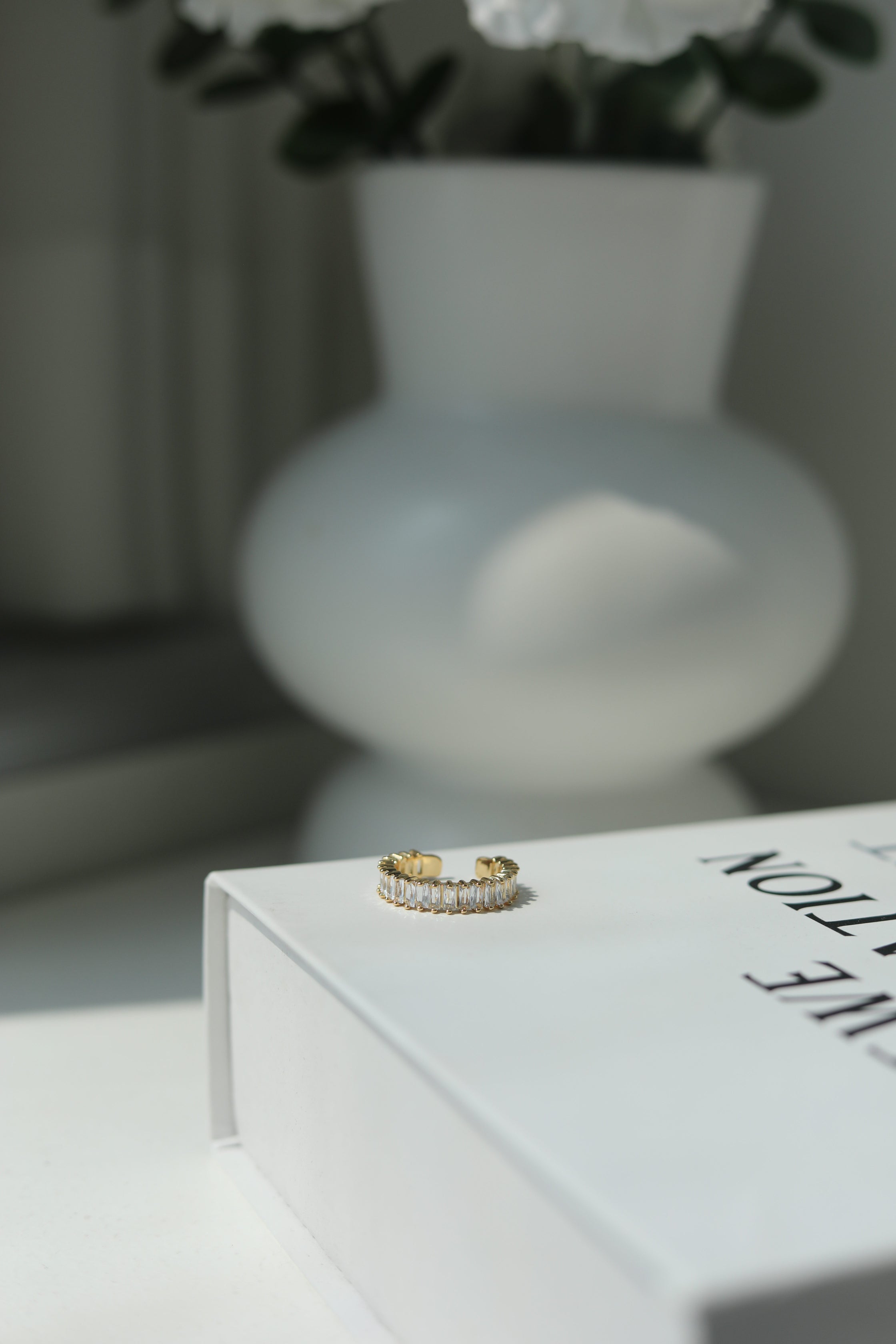Gold one size fits all ring on a book with a blurred vase and flowers in the background