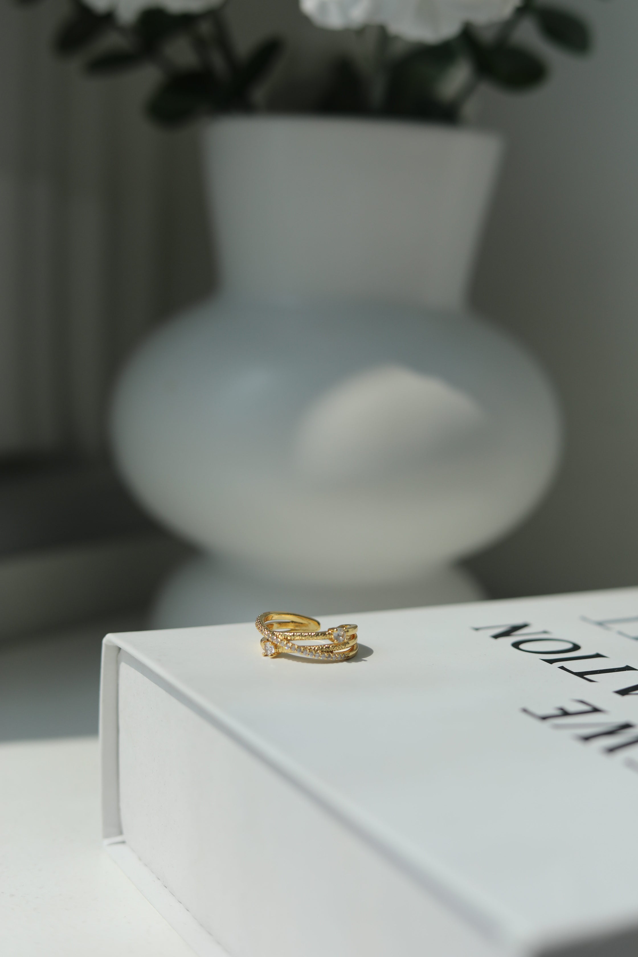 Gold ring on a white book with a blurred vase and flowers in the background