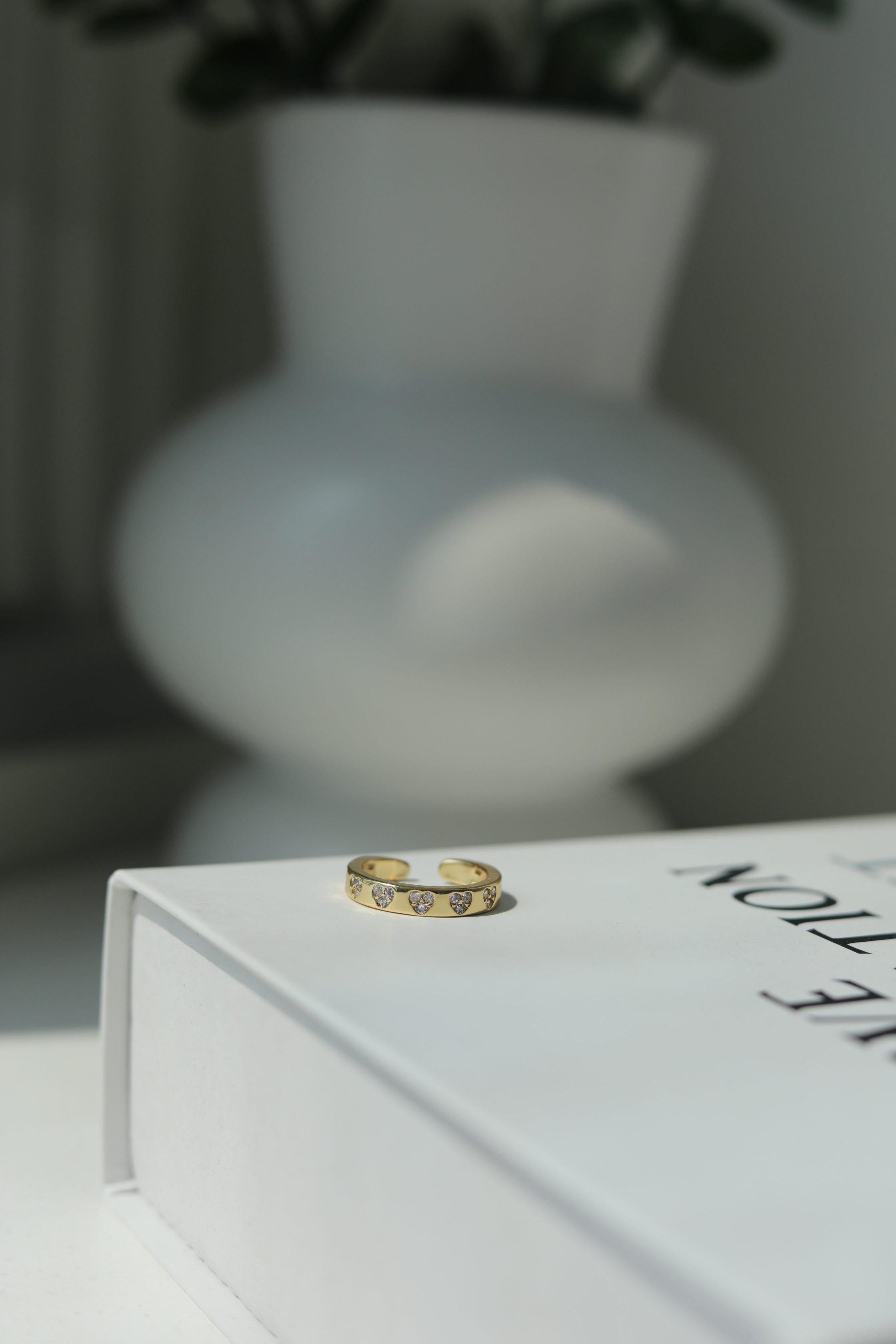 Gold ring on a white surface with a blurred vase in the background