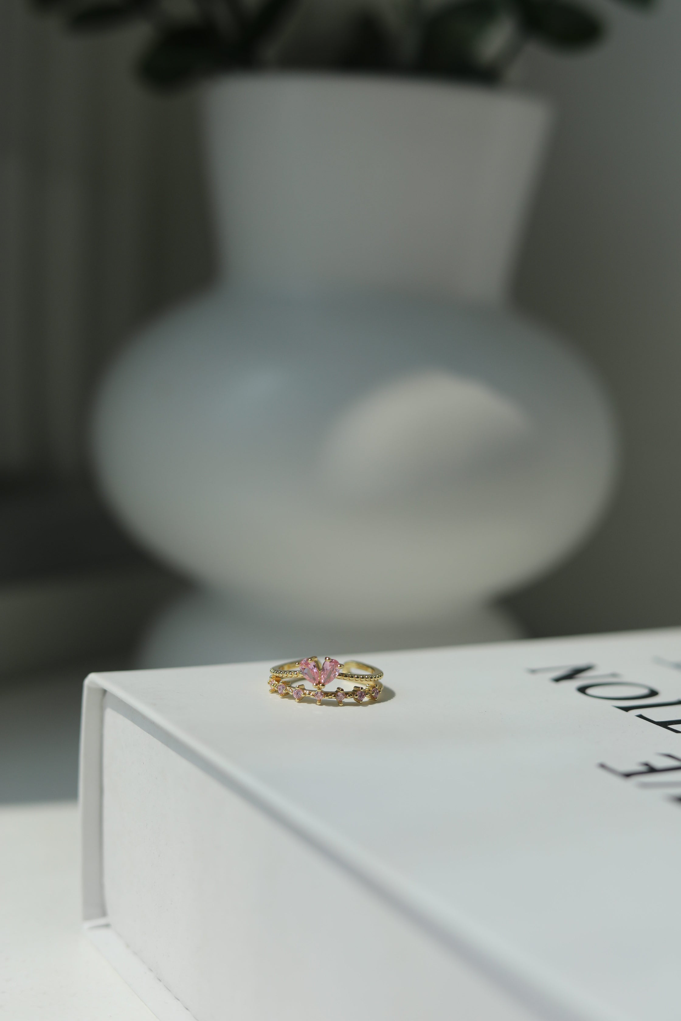 Girly old ring with a colorful pink heart gemstone on a white surface with a blurred vase in the background