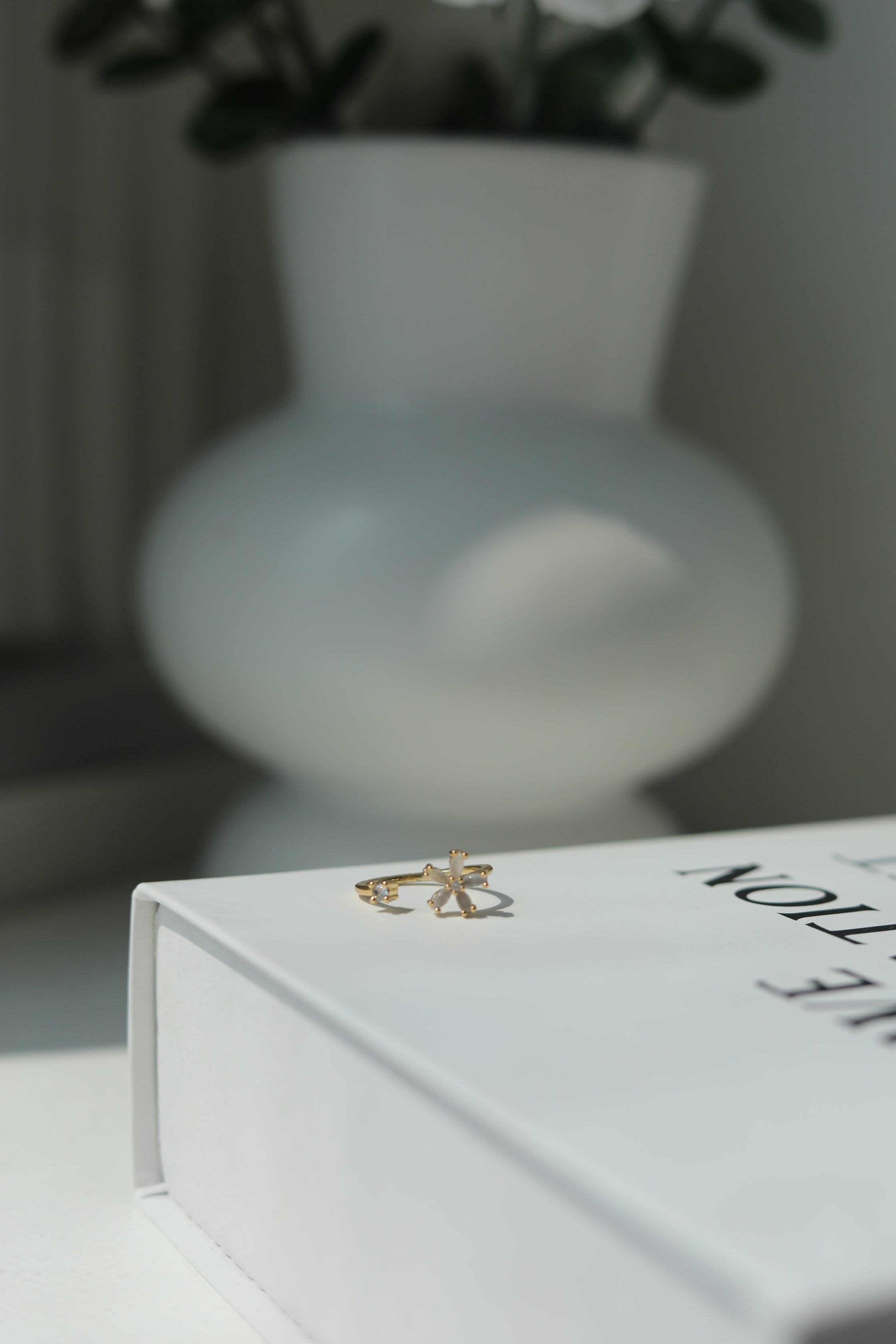 Gold ring on a white surface with a blurred vase in the background