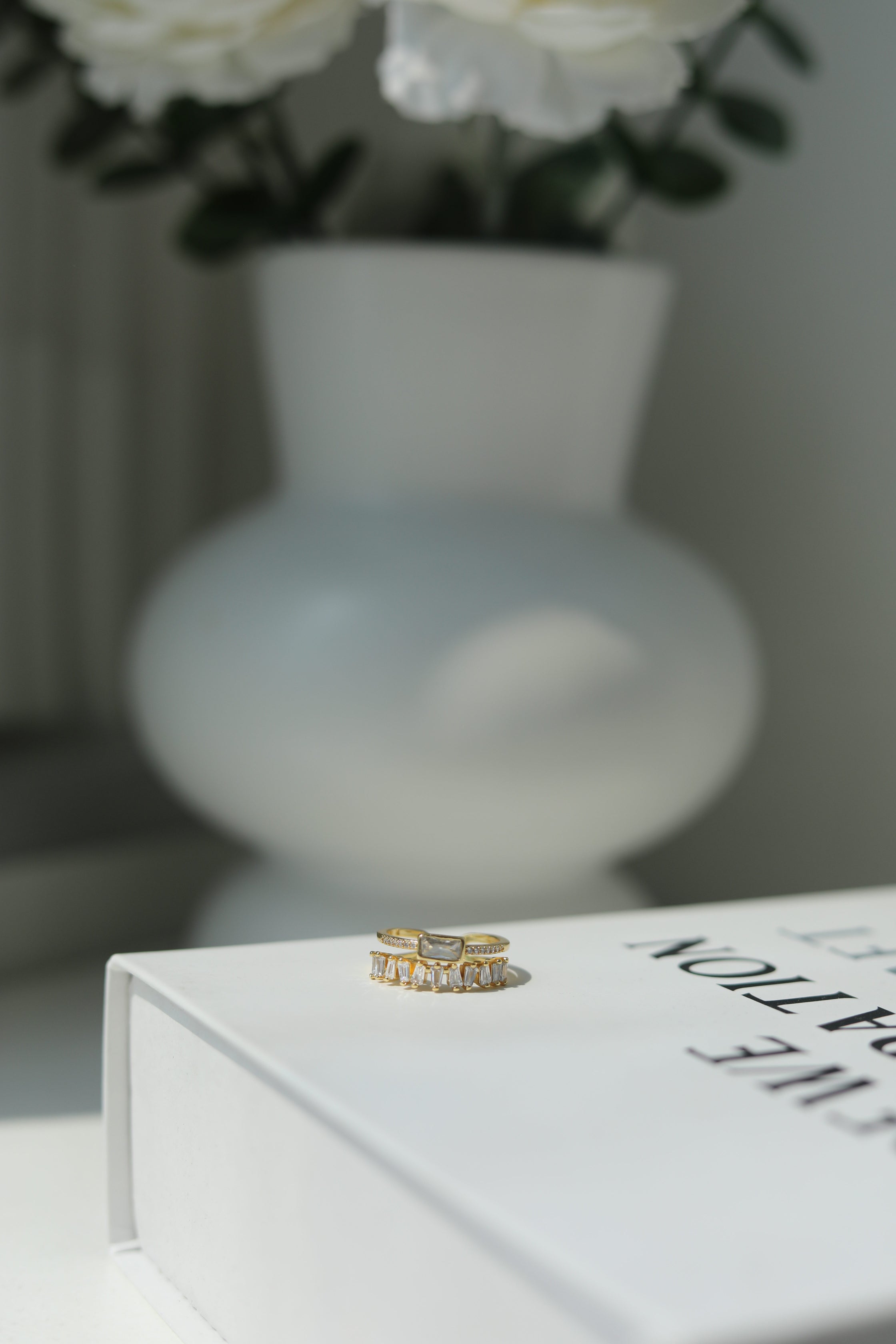 Gold ring on a white book with a blurred vase and flowers in the background