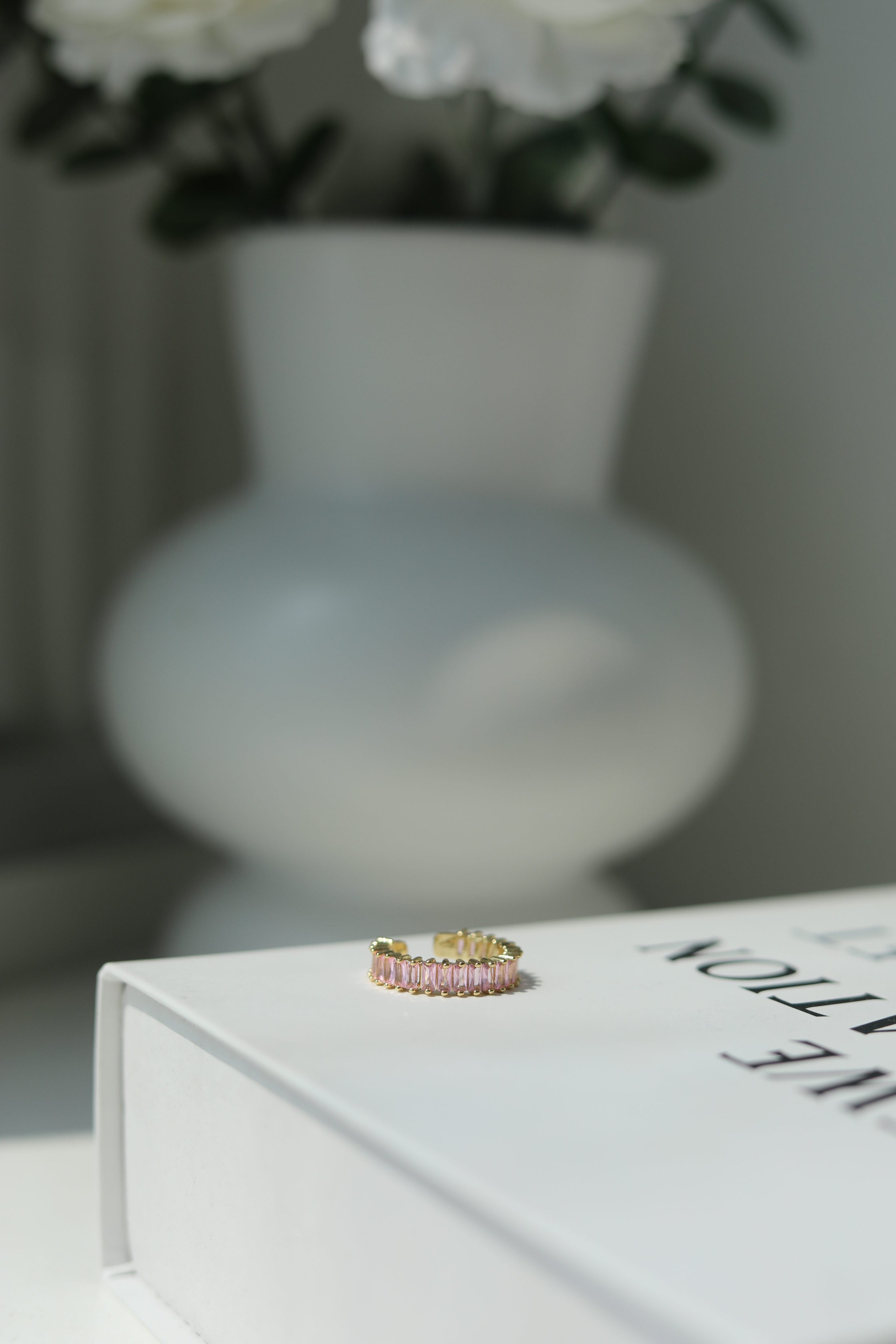 Pink ring on a book with a blurred vase and flowers in the background