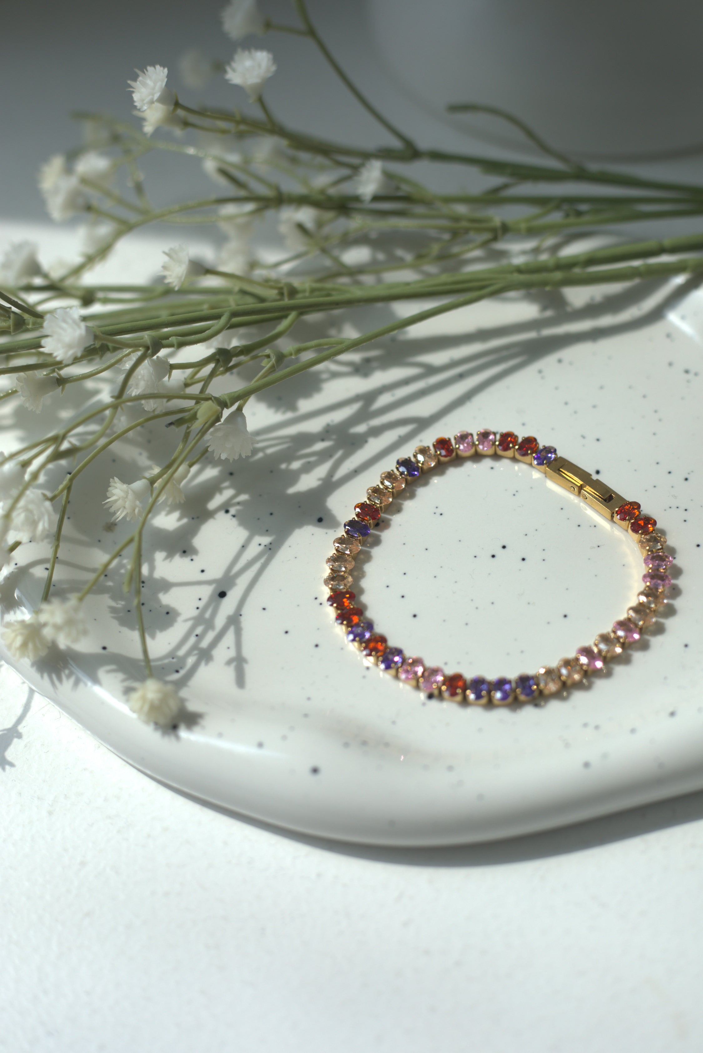 Multicolored beaded bracelet on a white plate with small white flowers