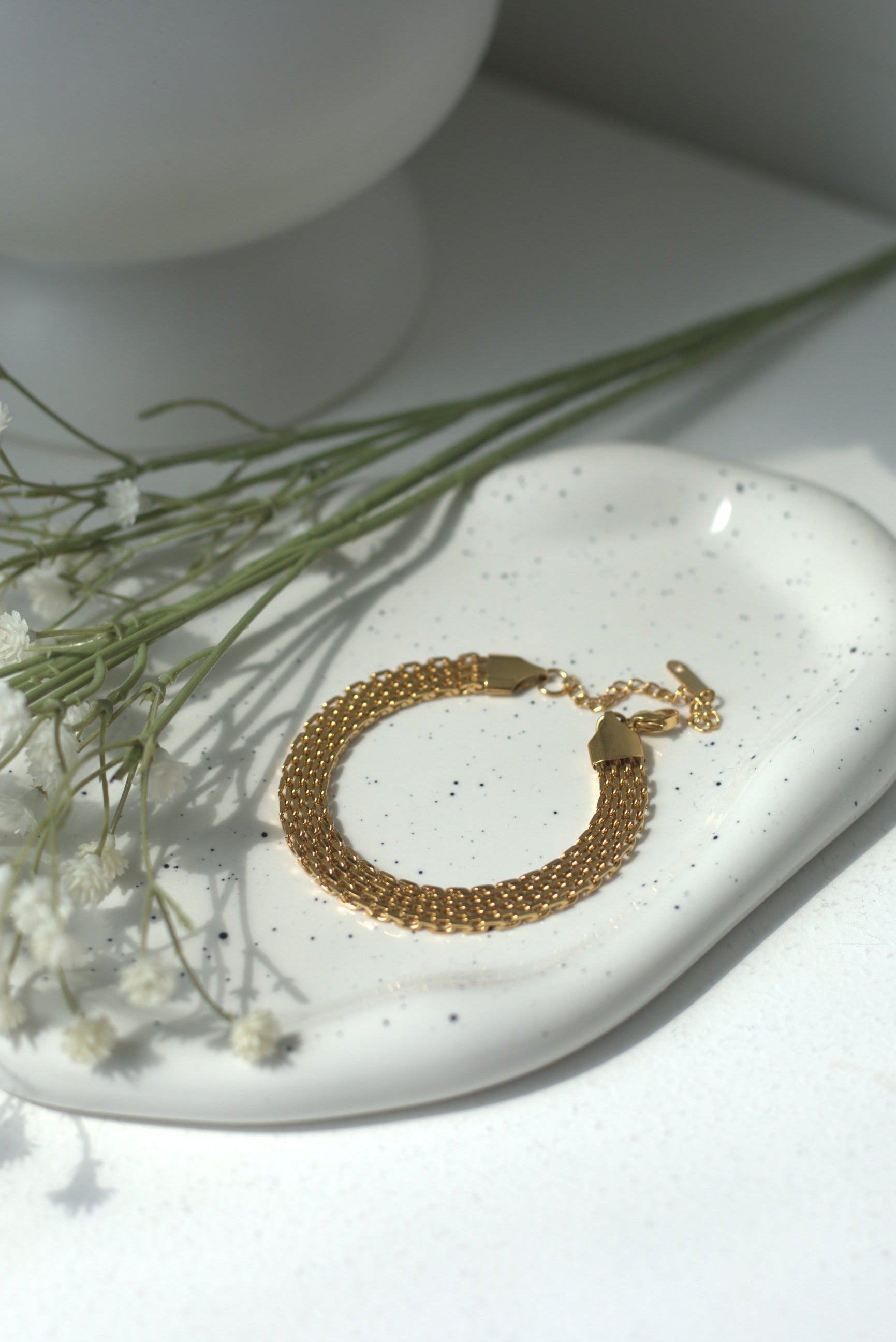 Gold bracelet on a white ceramic dish with small flowers, against a light background