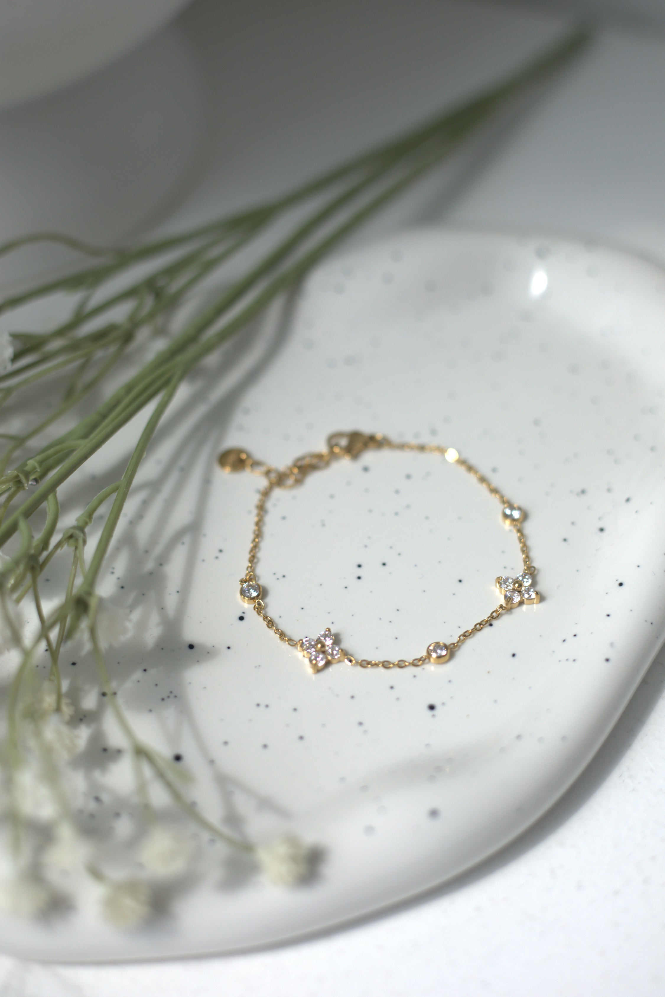 Dainty gold bracelet on a white speckled dish with delicate greenery