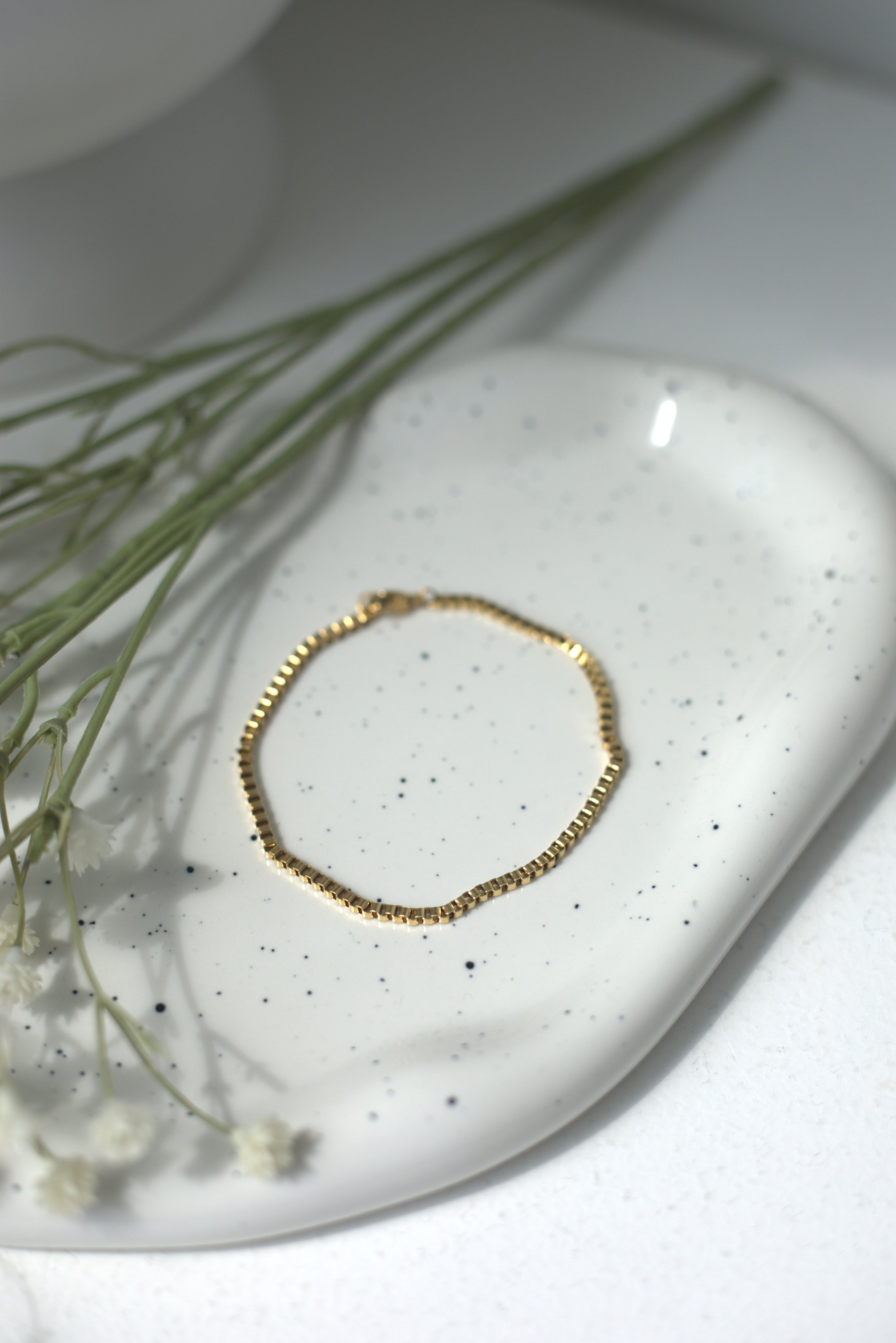 Gold bracelet on a white speckled dish with greenery