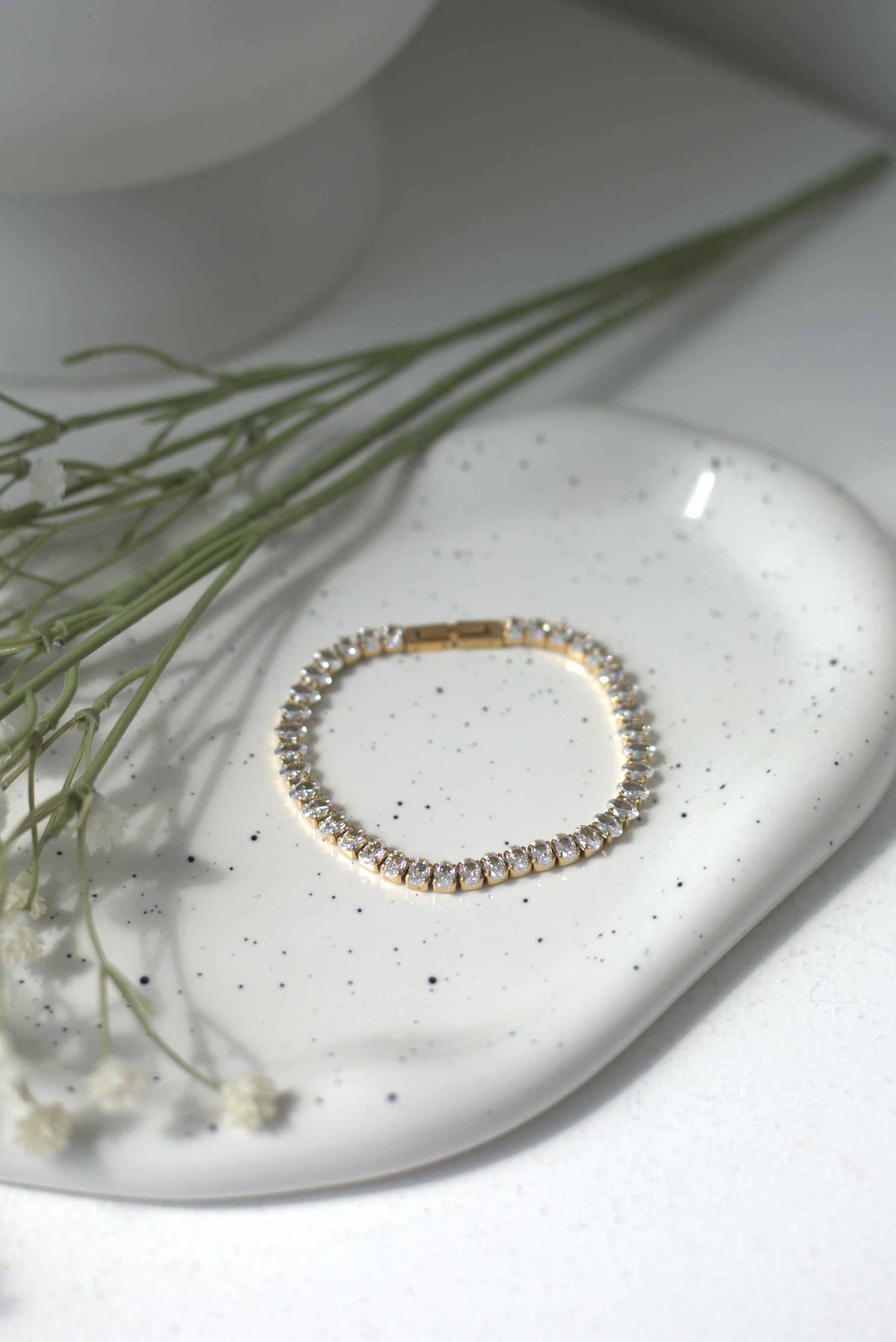 Gold bracelet on a white ceramic dish with greenery