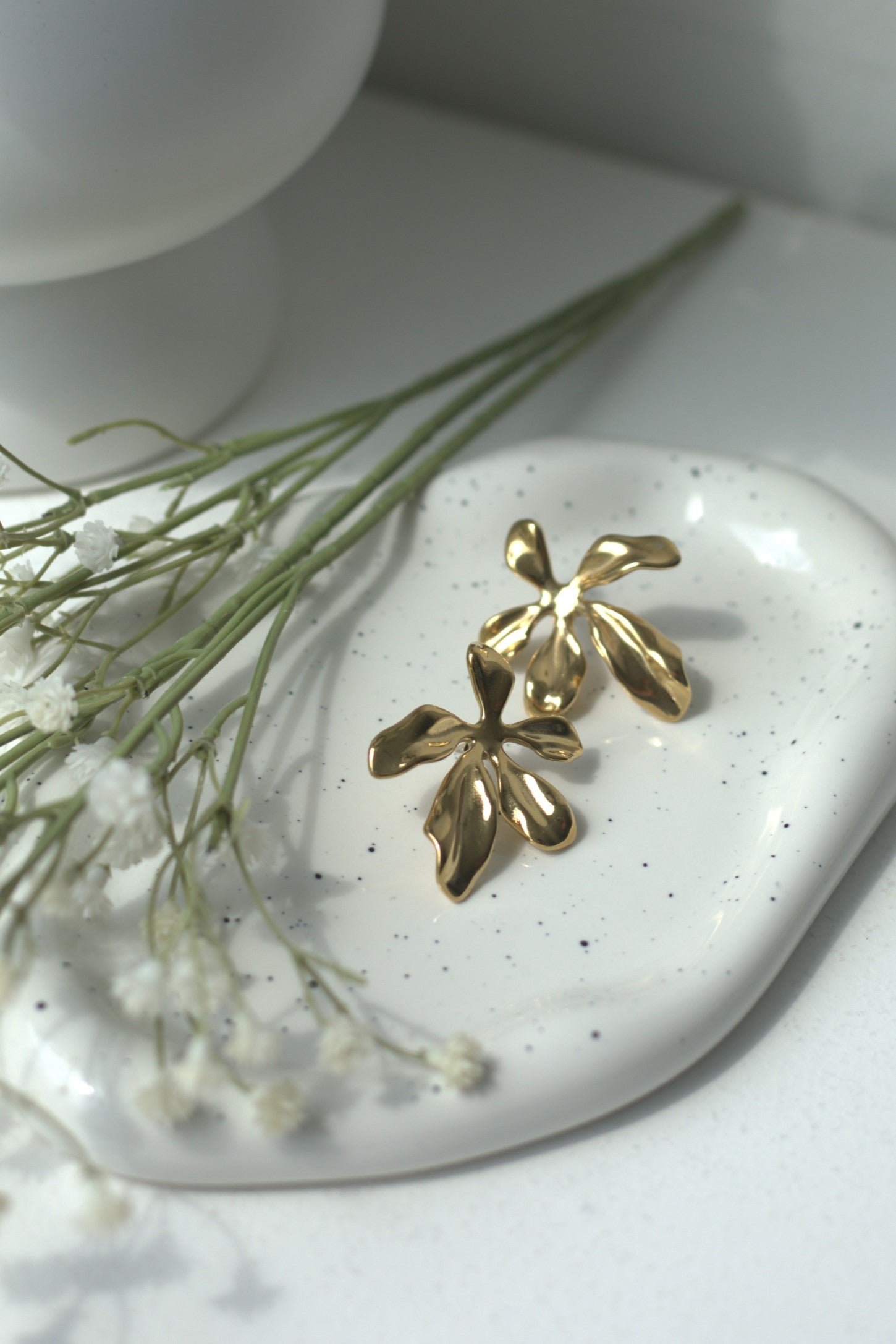 Bold statement gold flower / leaf earrings on a white stone with greenery
