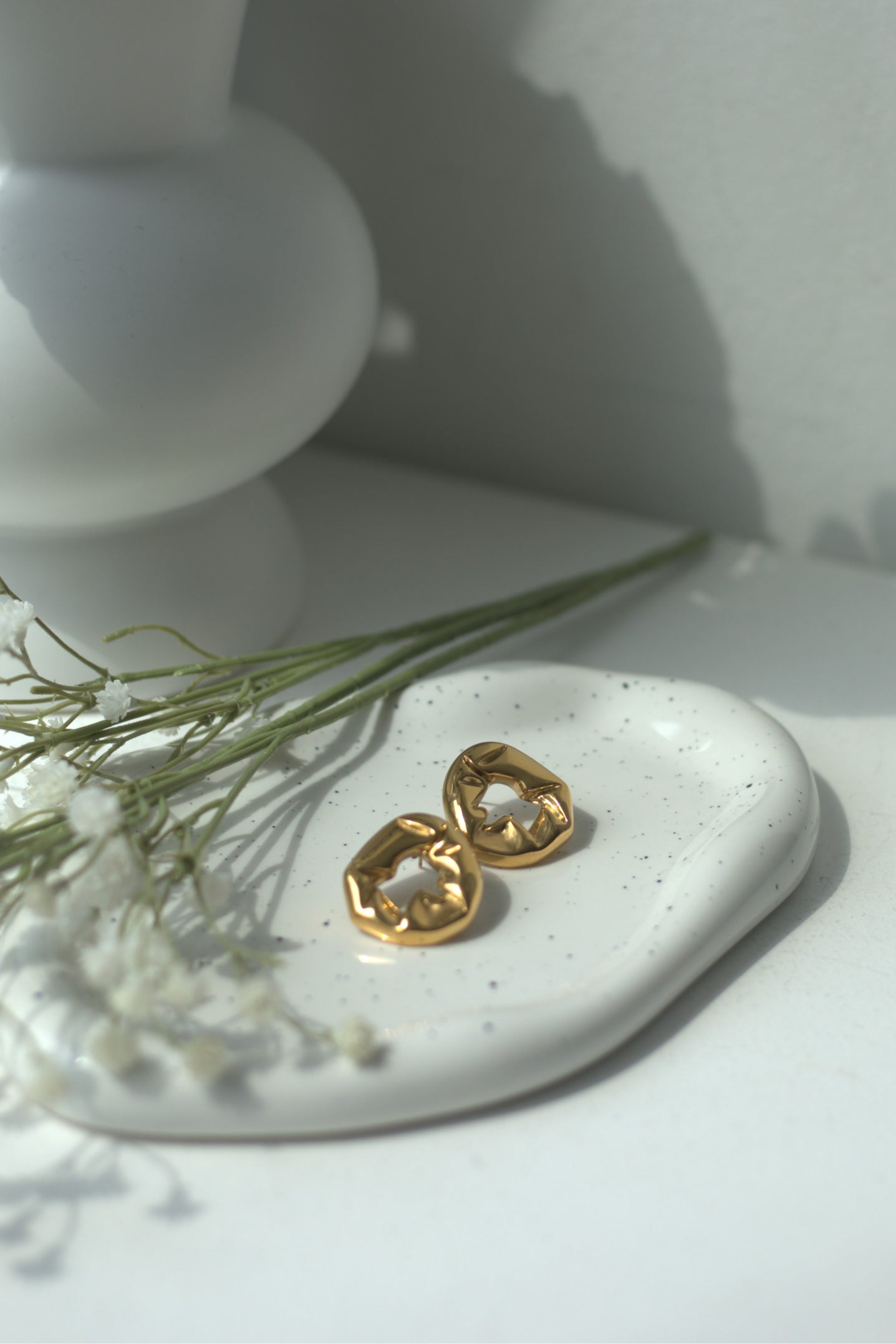 Gold statement earrings on a white surface with a minimal background