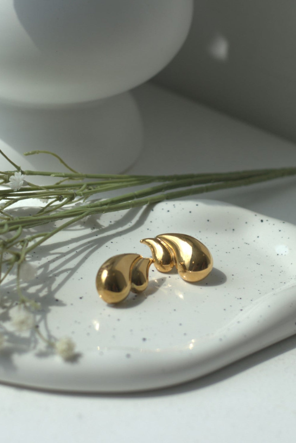 Gold teardrop earrings on a white ceramic dish with a white background
