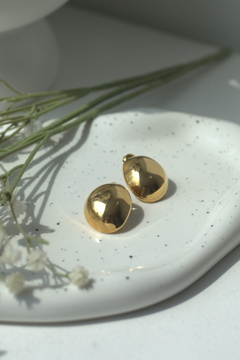 Gold waterproof earrings on a white ceramic dish with small flowers