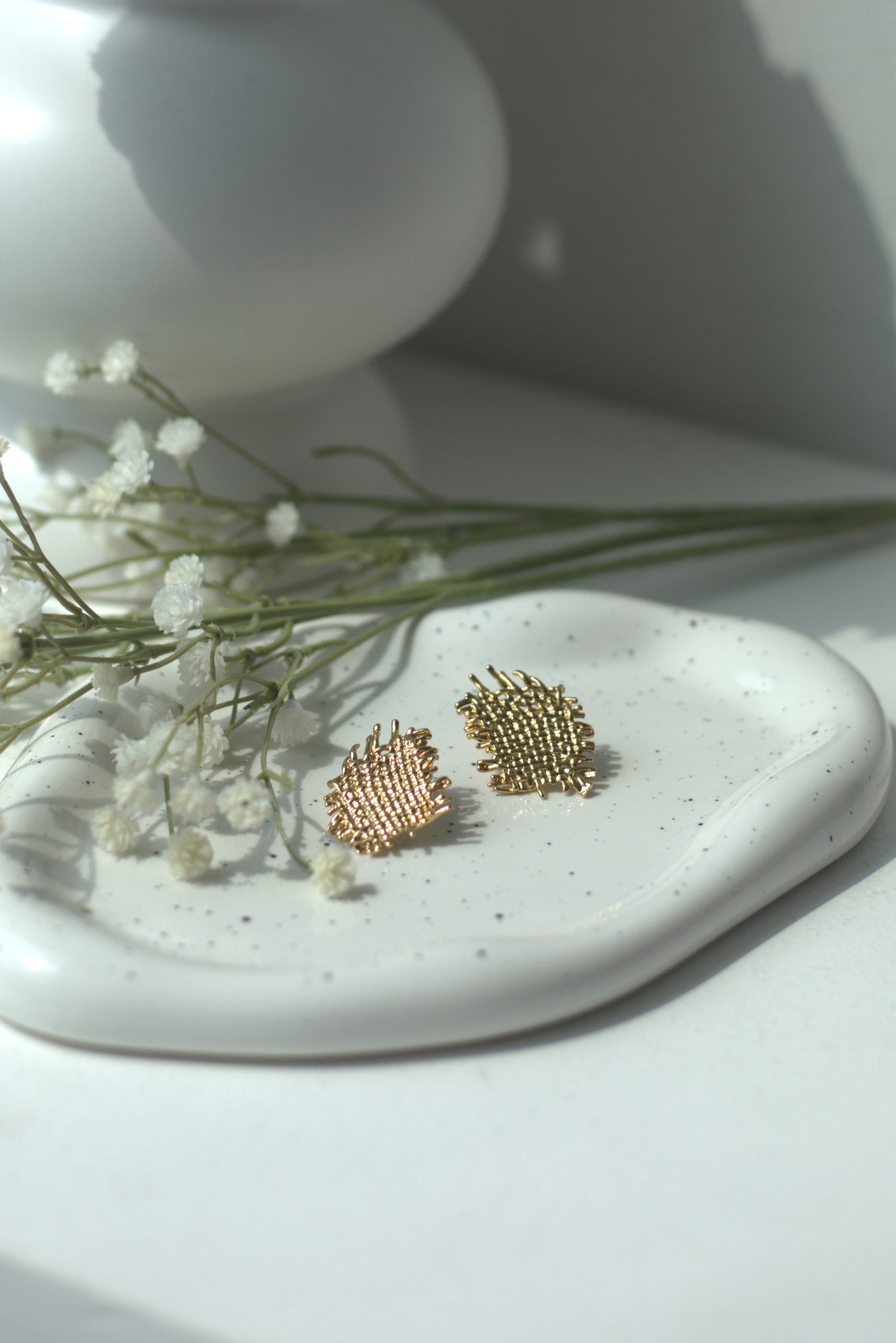 Gold earrings on a white ceramic dish with small white flowers