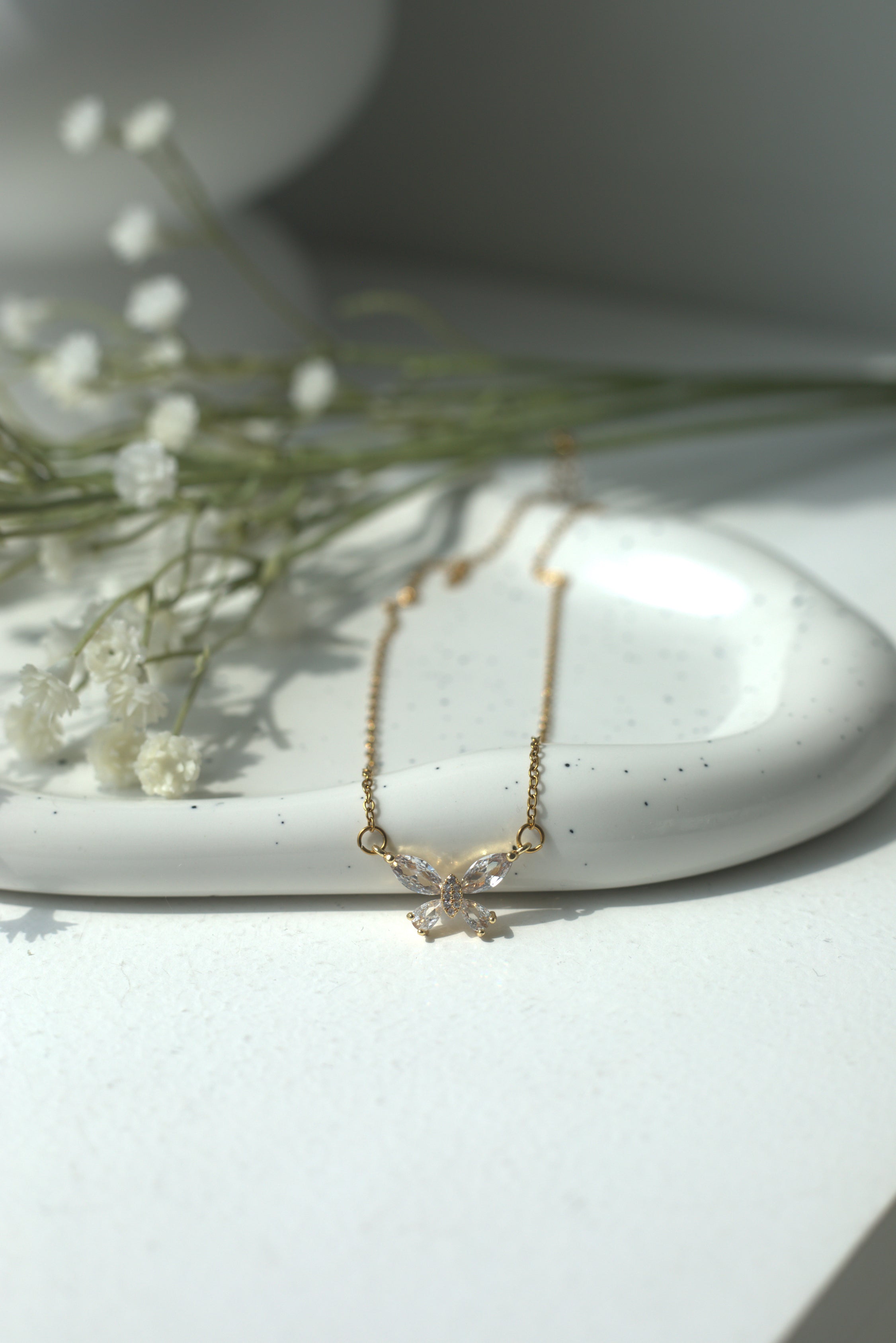 Gold butterfly necklace on a white dish with dried flowers