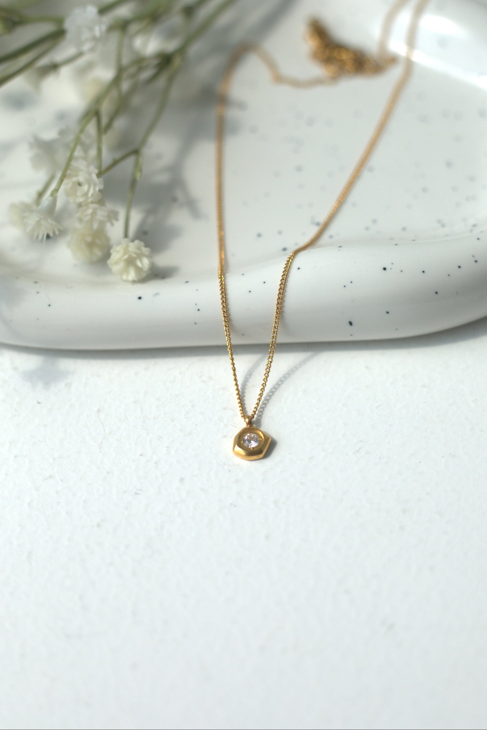 Gold necklace on a white surface with dried flowers in the background
