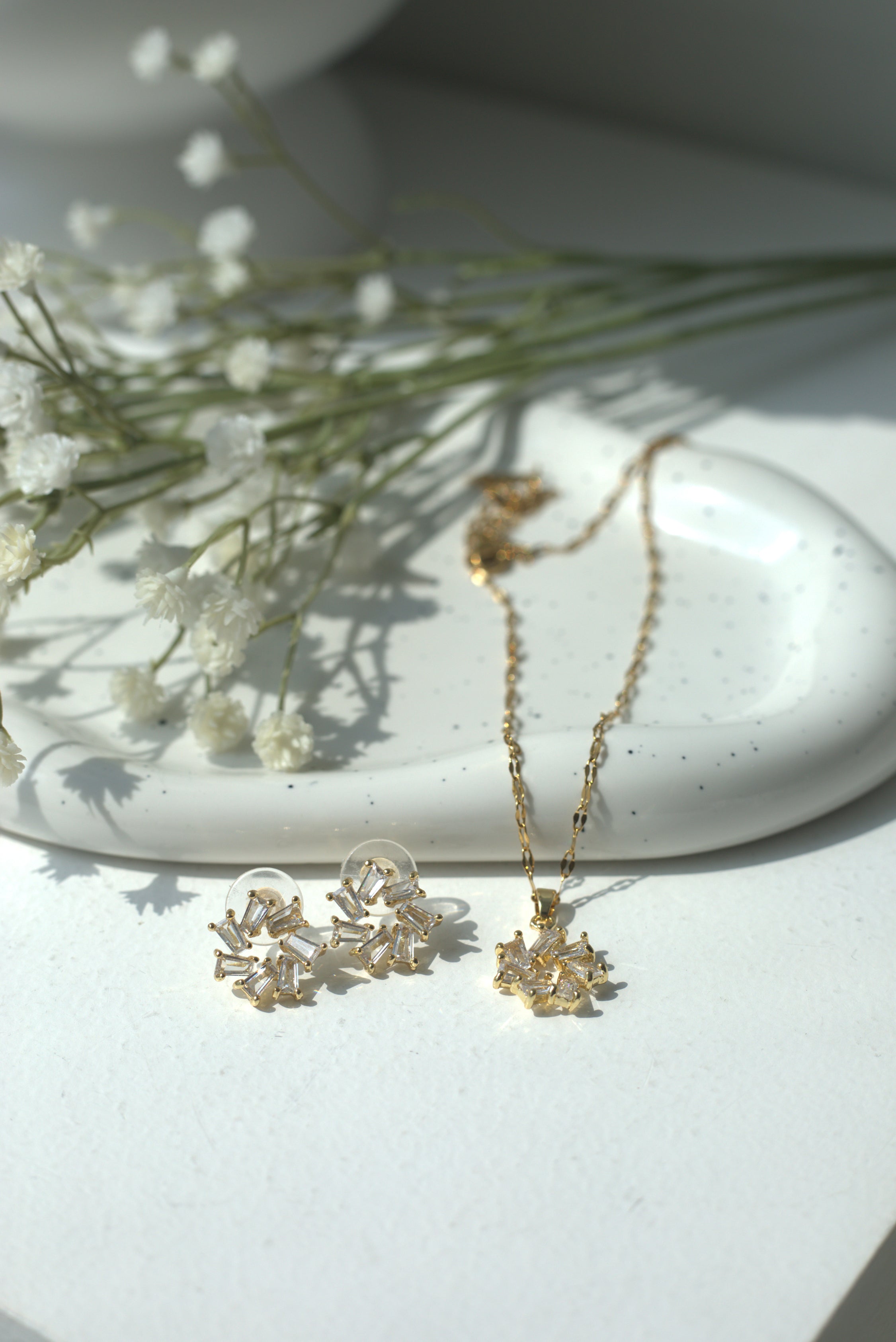 Gold necklace and earrings on a white surface with small white flowers.