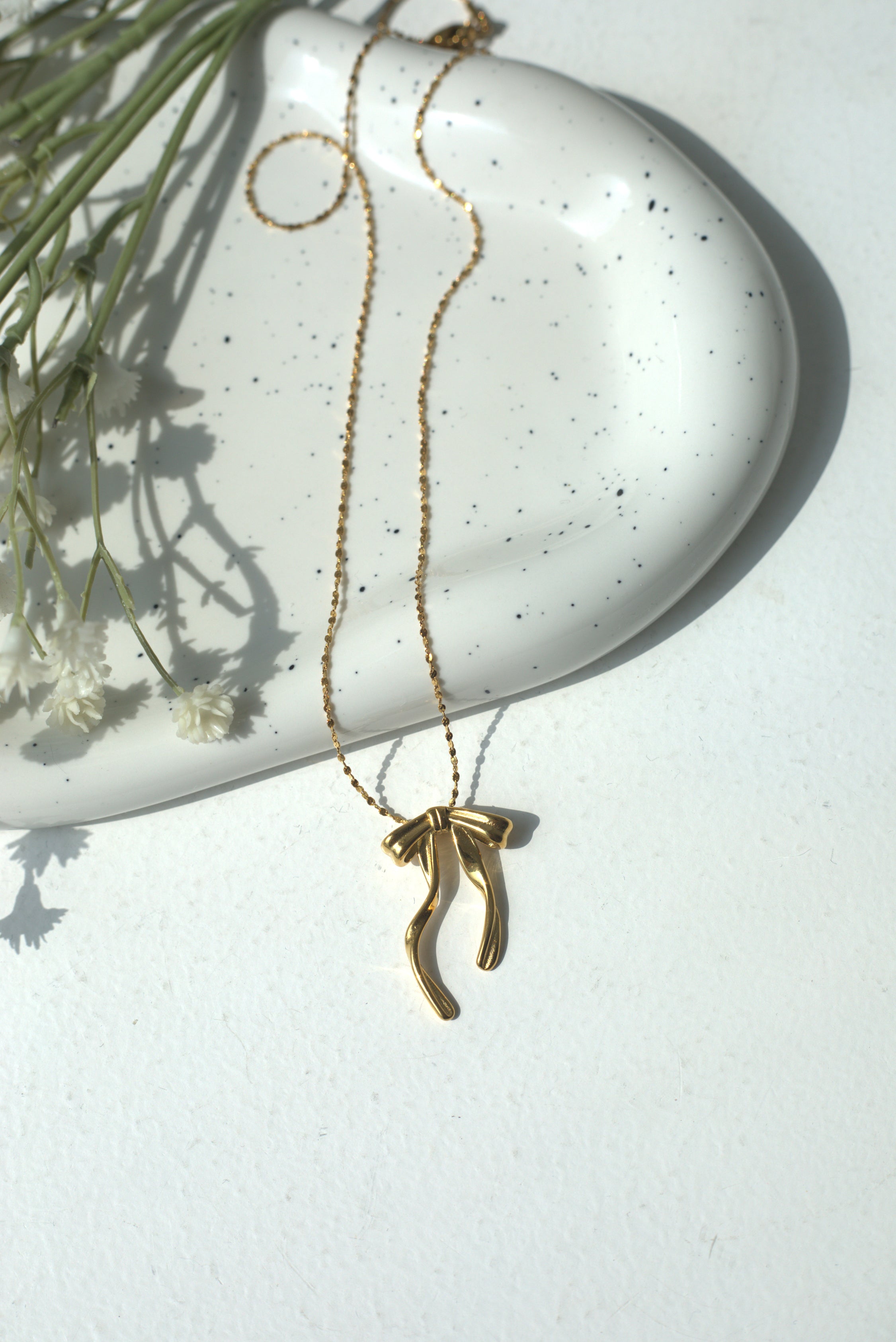 Gold necklace with a unique pendant on a white surface with dried flowers.