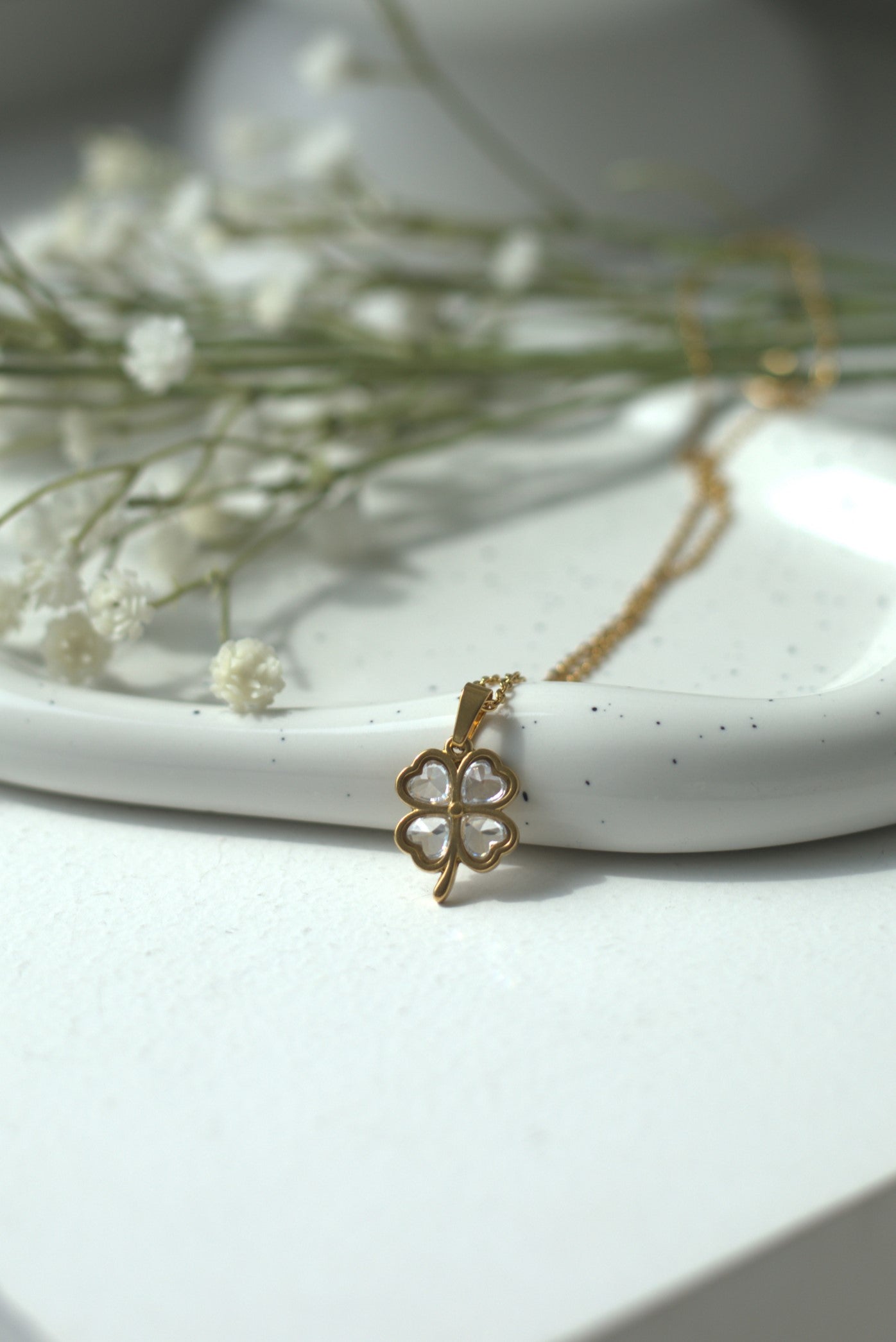 Gold four leafed clover good luck necklace with a clover pendant on a white surface with dried flowers.