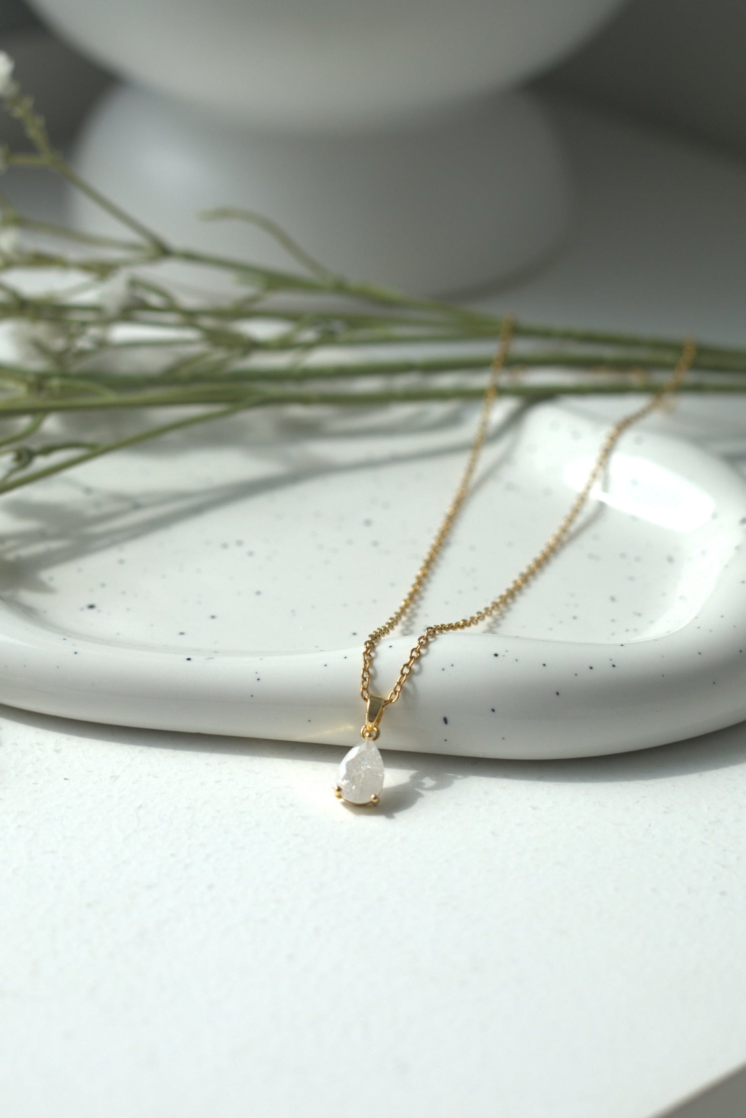 Gold necklace with a pendant on a white ceramic dish with small flowers.