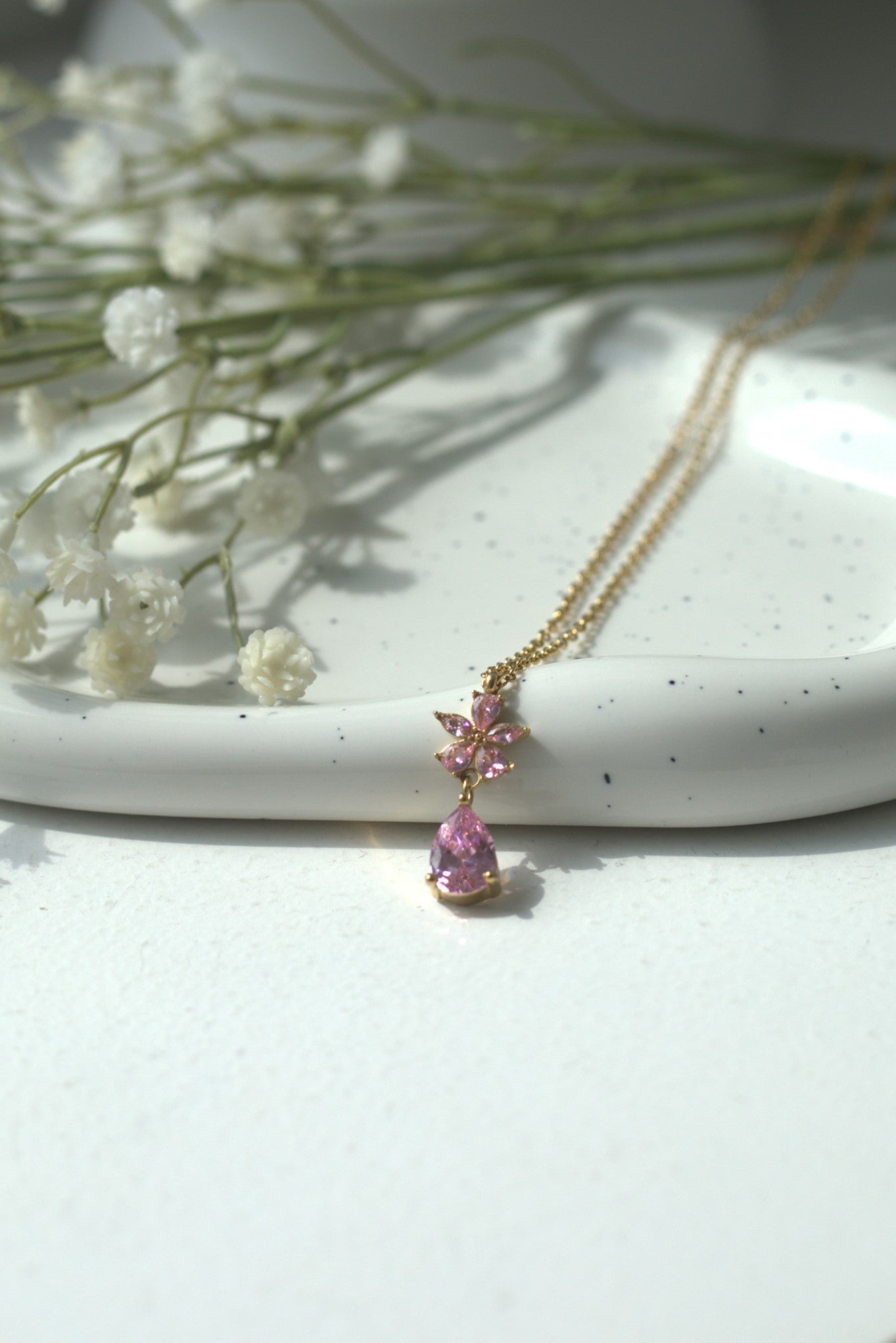 Necklace with pink teardrop pendant on a white surface with small white flowers