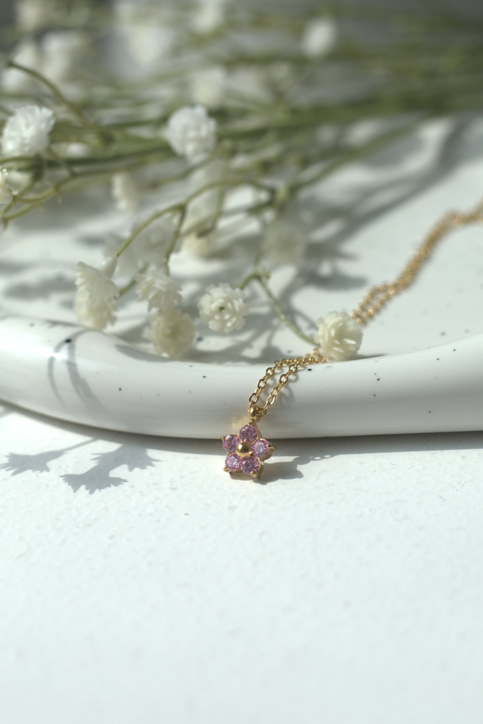 Necklace with a pink pendant on a white surface with dried flowers.
