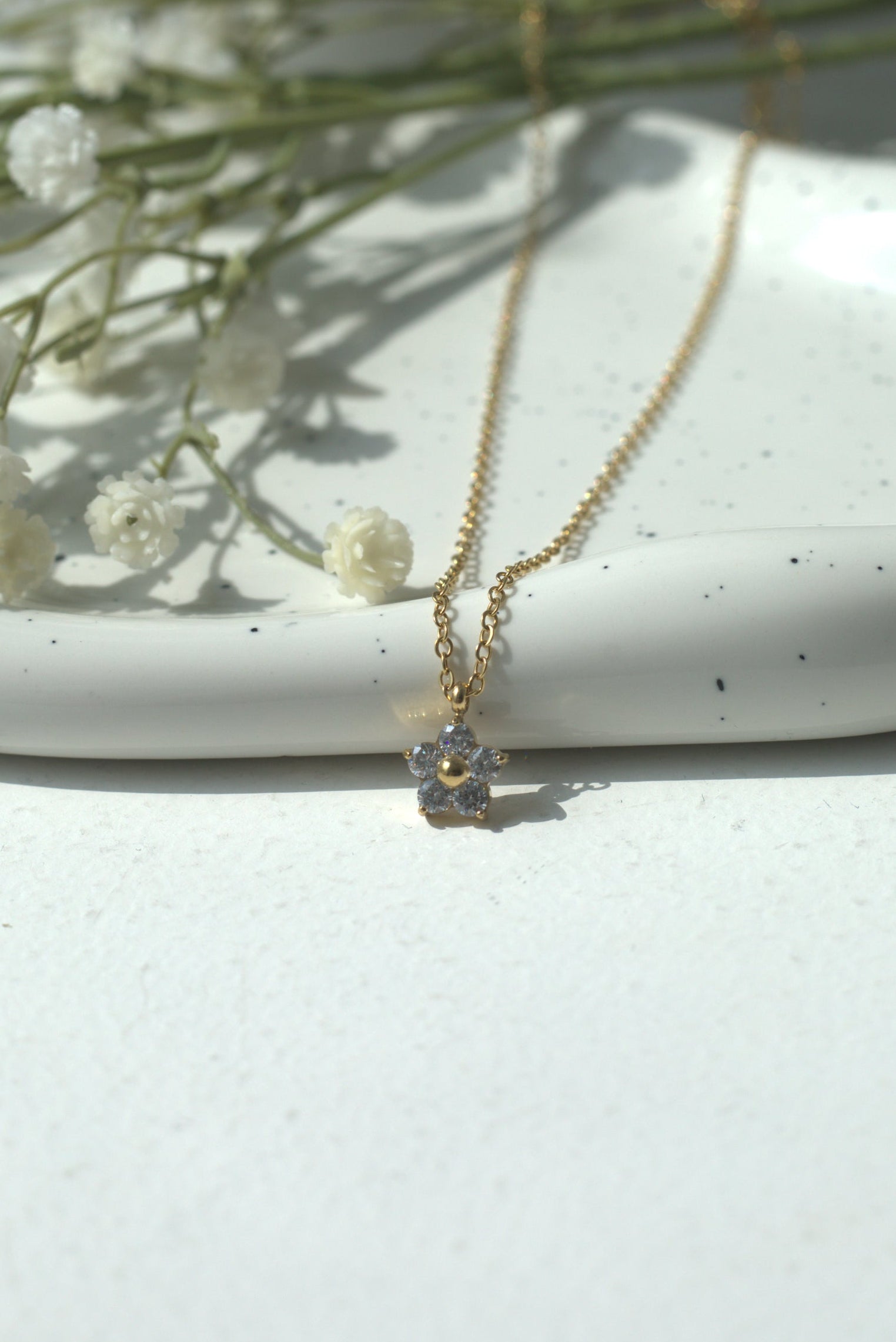 Gold waterproof necklace with a delicate pendant on a white surface with baby's breath flowers.