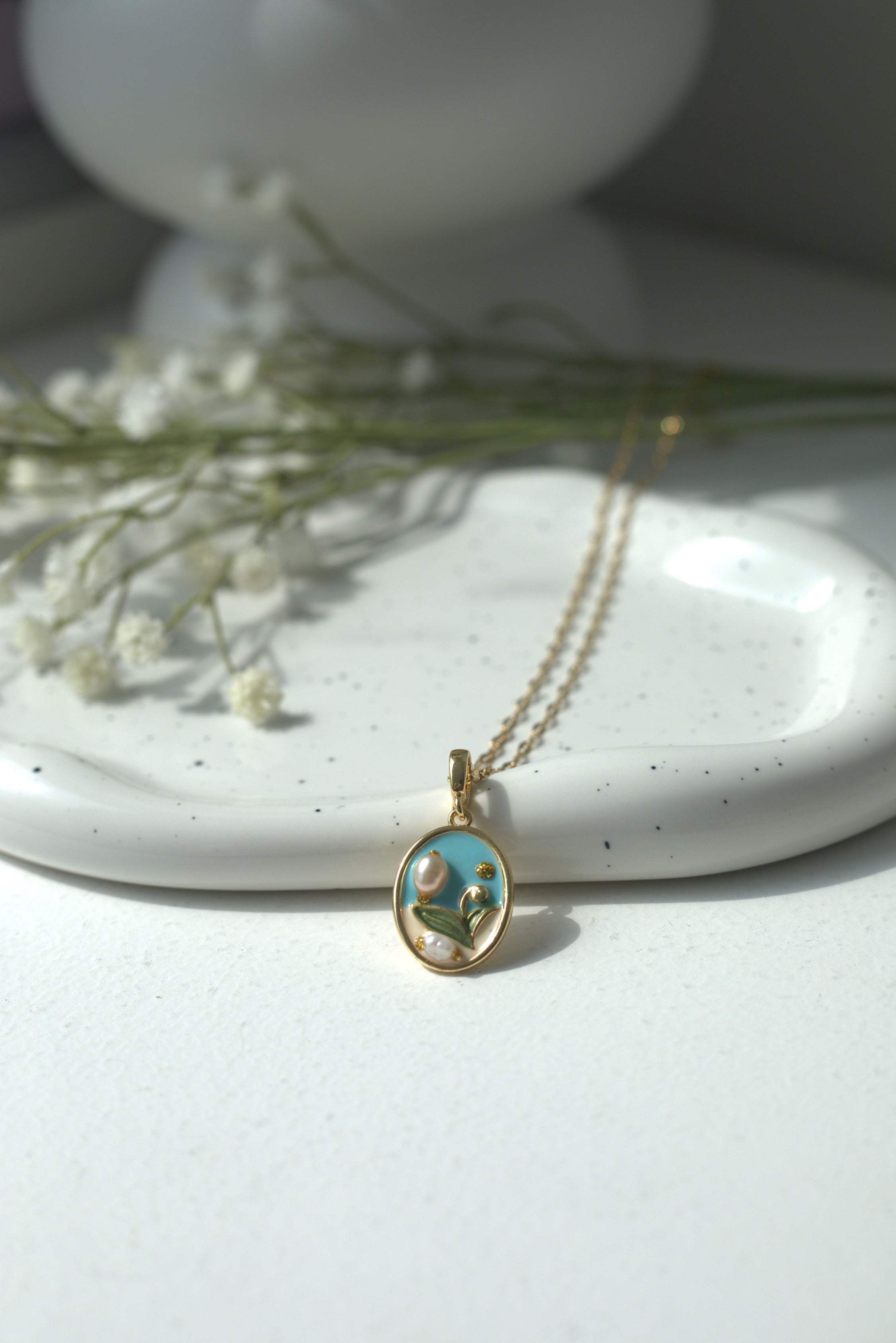 Gold necklace with a pendant on a white surface with flowers in the background