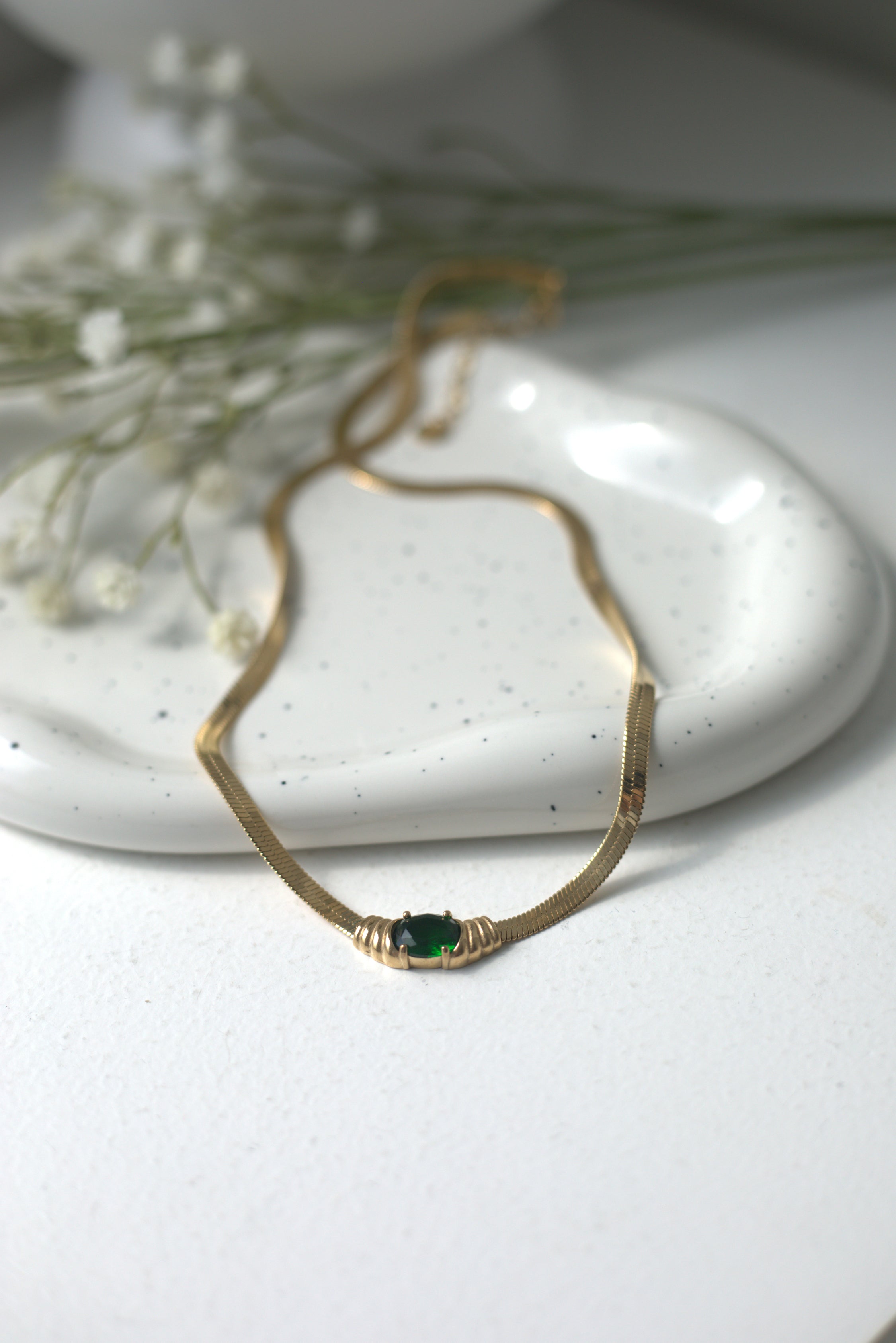 Gold necklace with a green gemstone on a white surface