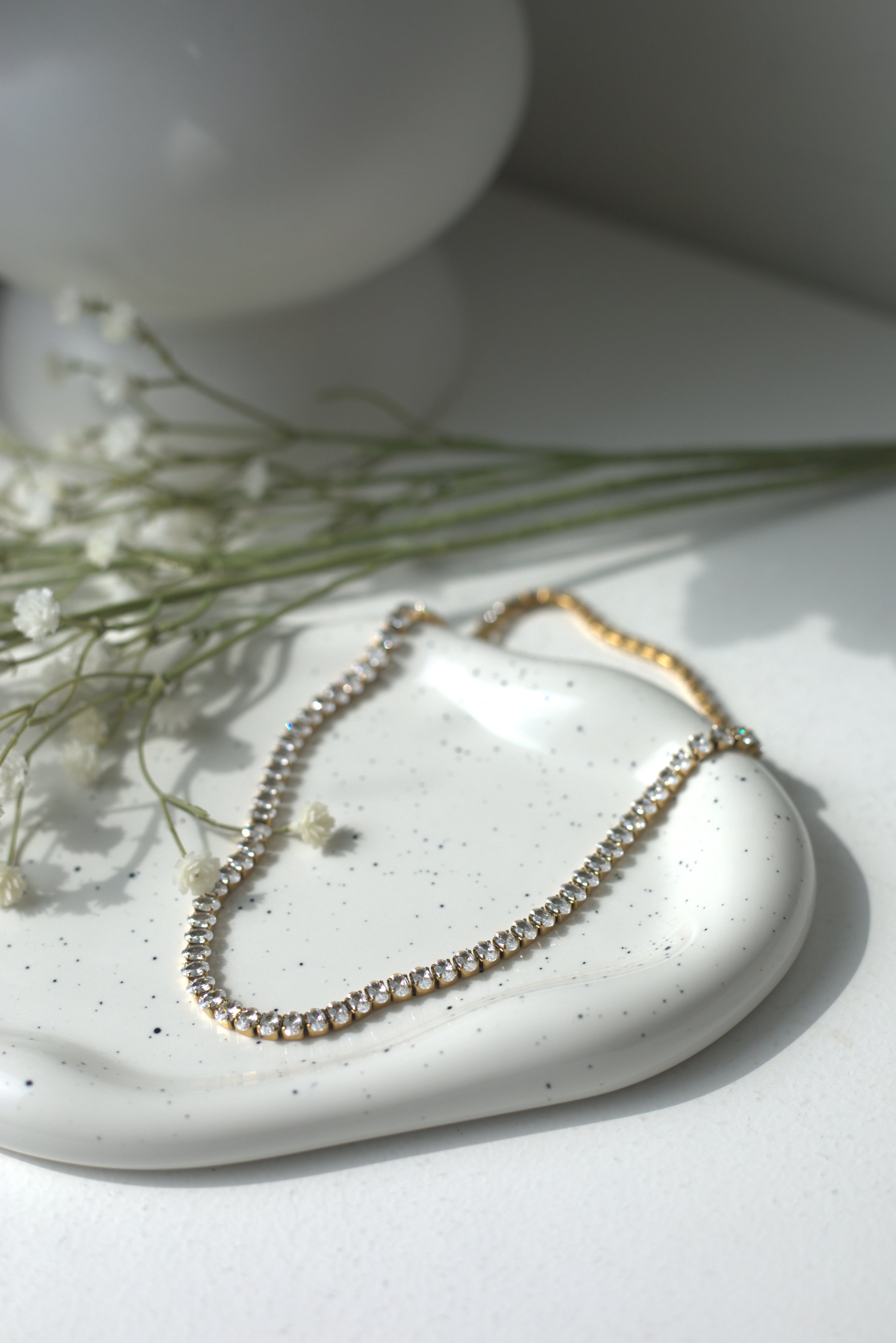 Necklace with small stones on a white ceramic dish with greenery