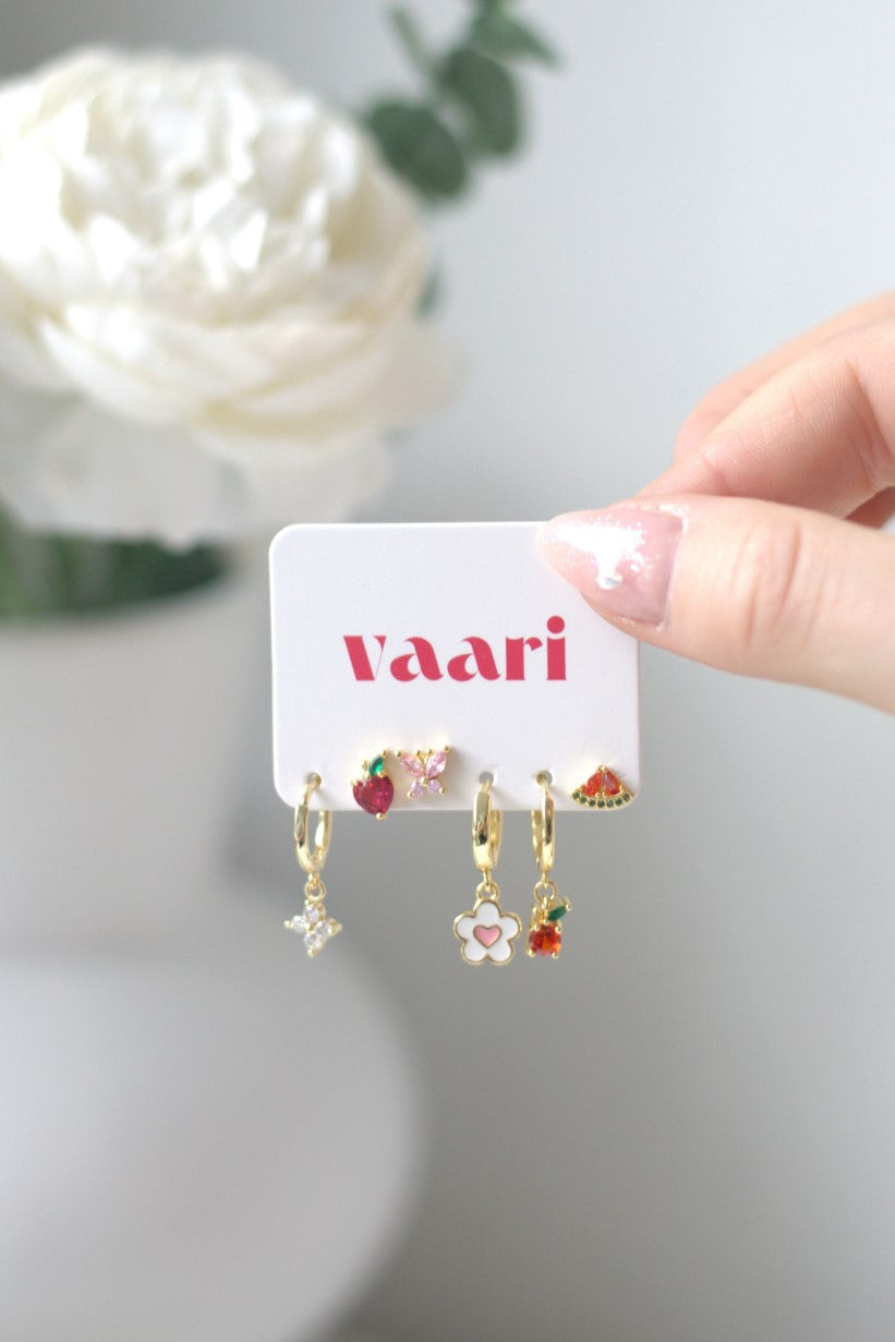 Hand holding a card with waterproof earrings in flower, watermelon, apple and peach designs and 'vaari' branding against a light background