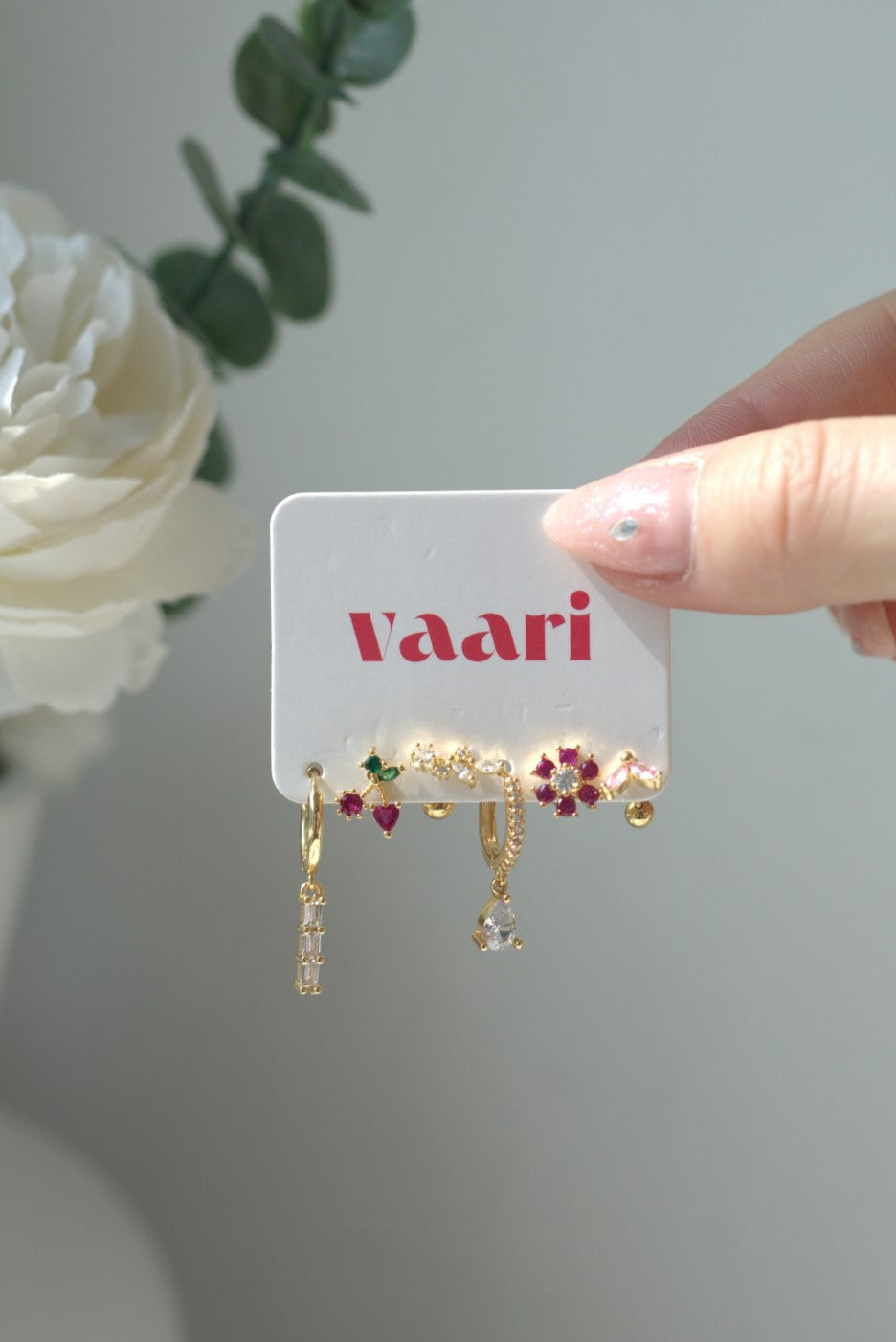 Gold earrings on a 'vaari' branded card with a white flower in the background