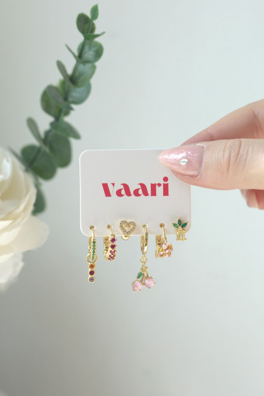 Set of gold earrings on a 'Vaari' branded card held by a hand with pink nail polish.