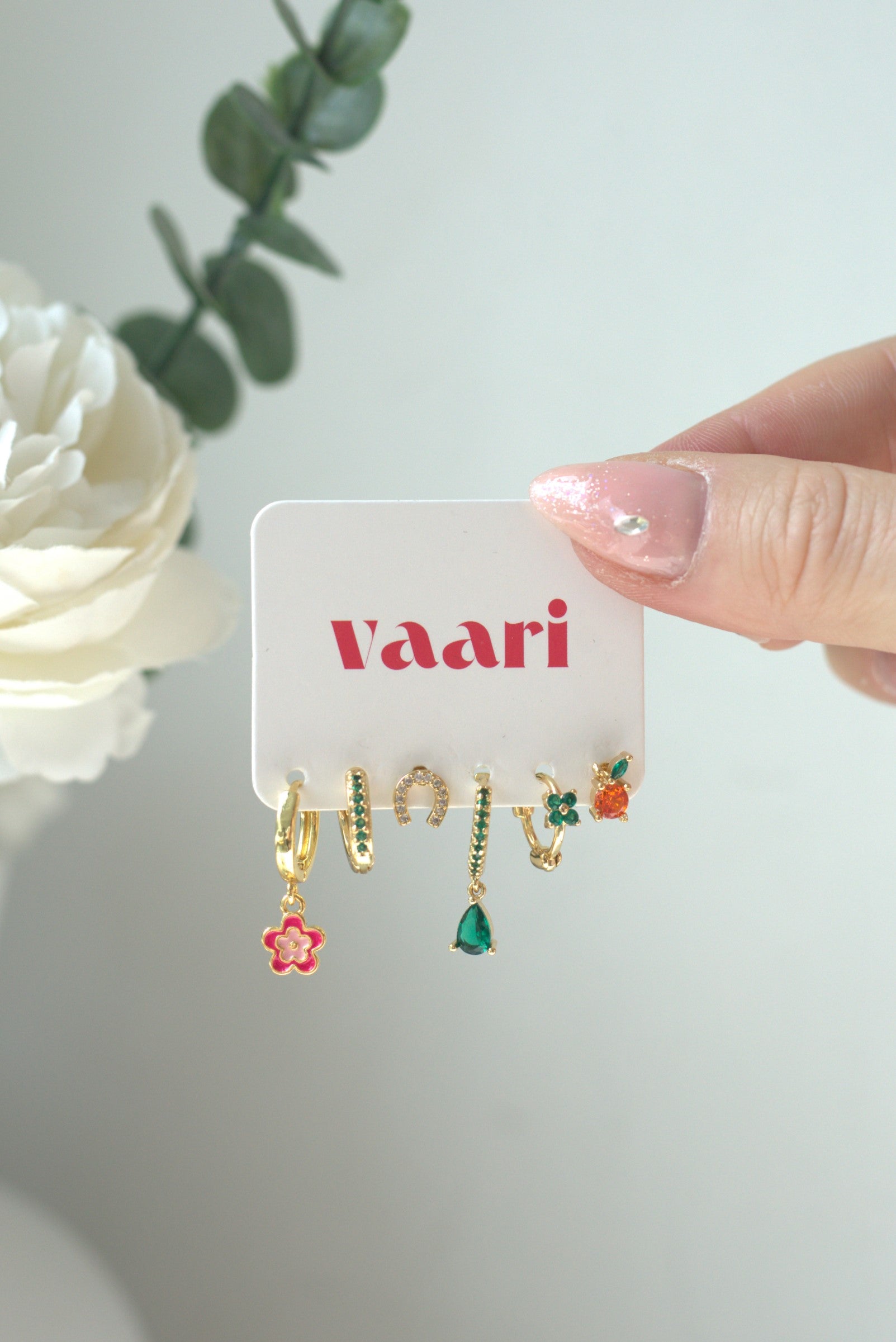 Set of green, red and orange earrings in flower an fruity mandarin design on a 'Vaari' branded card with a white flower in the background