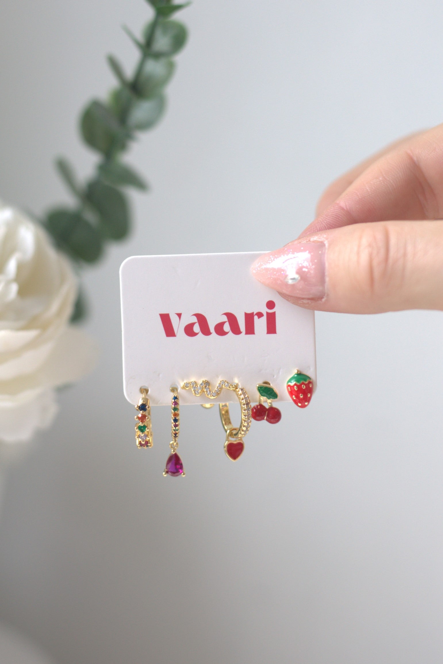 Earrings with colorful cherry, heart, snake and strawberry stones on a card held by a hand, with a blurred background