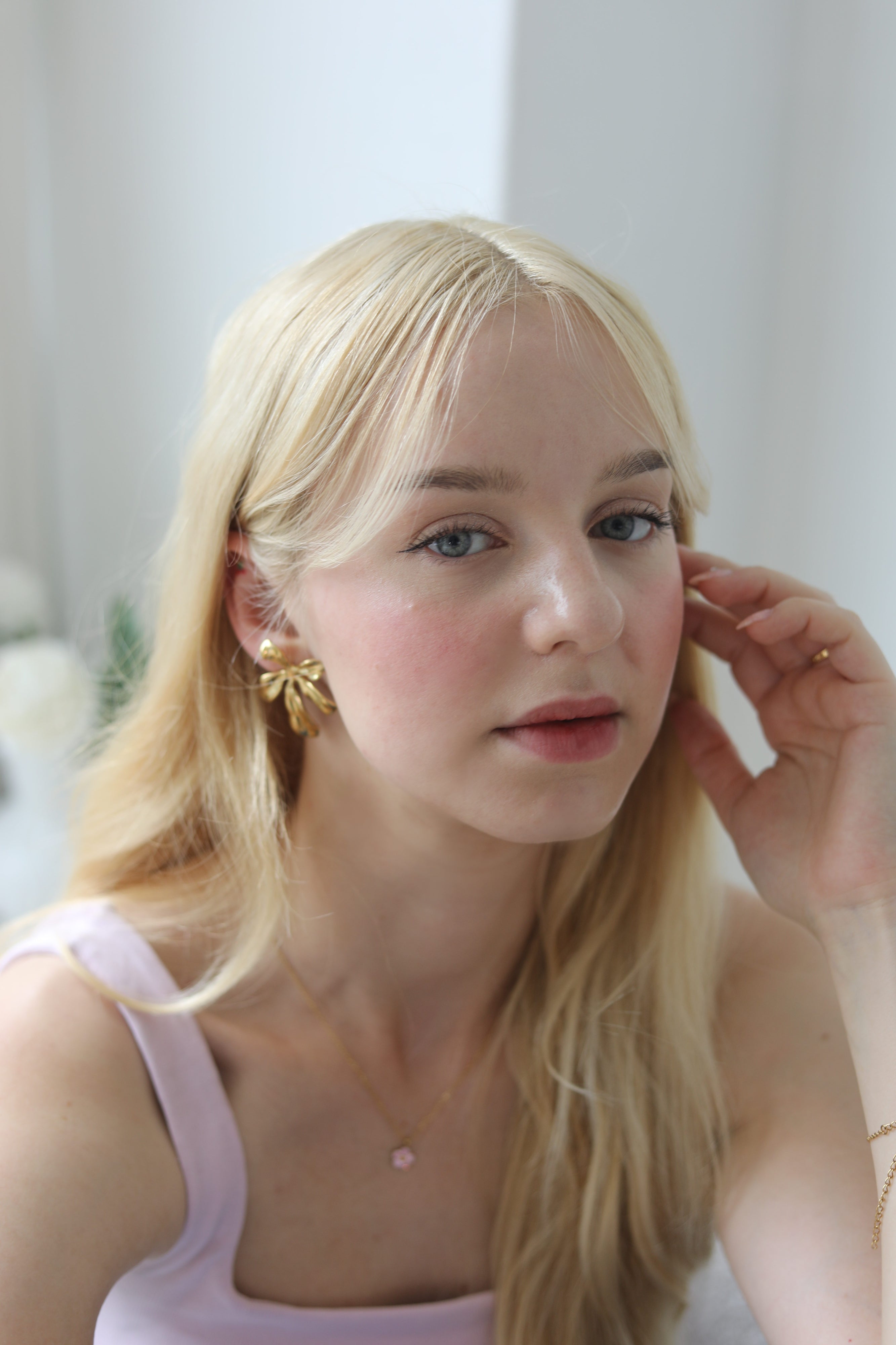 Blonde girl wearing pink showcasing a big pair of golf flower earrings and a delicate necklace.