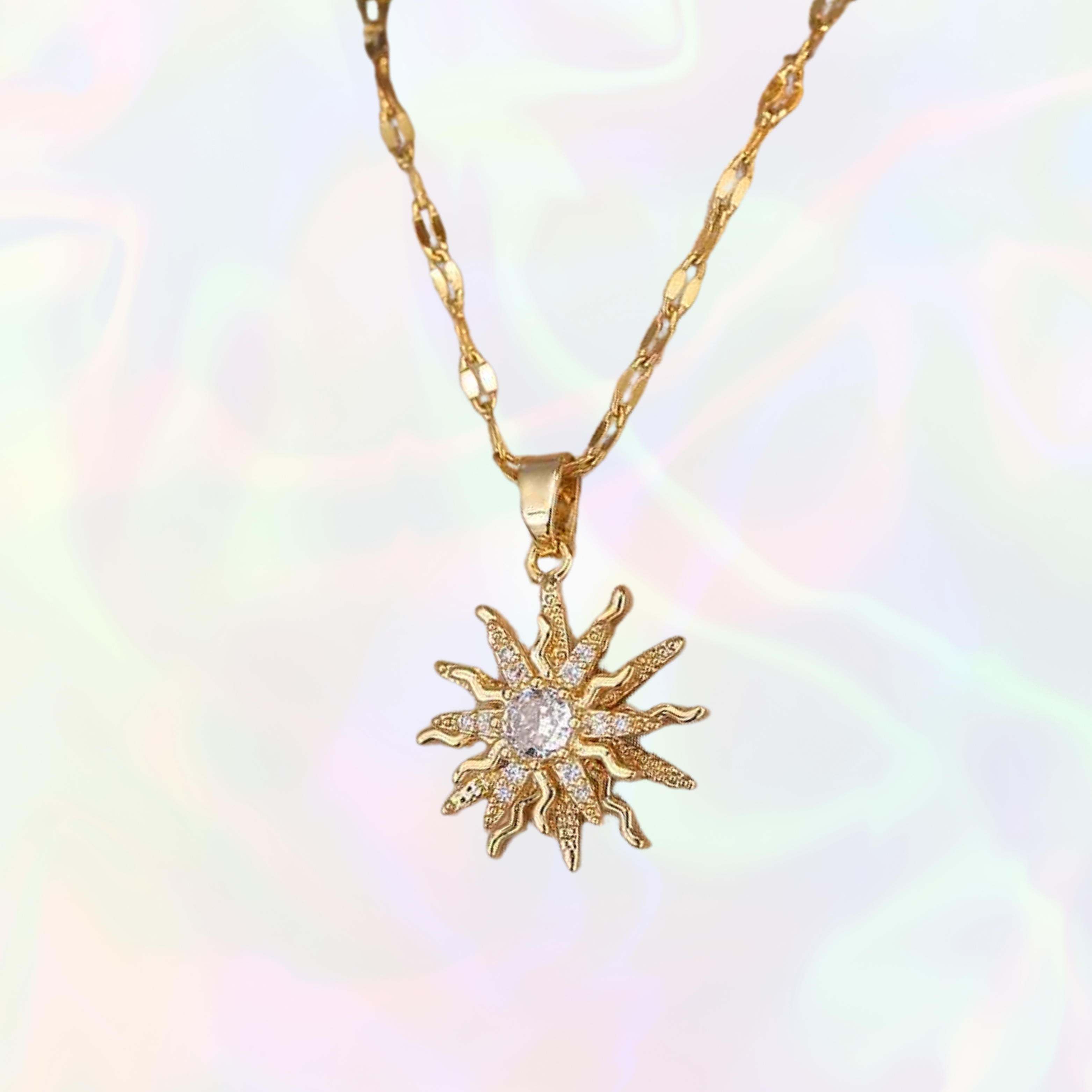 Gold sun-shaped pendant necklace on a soft, multicolored background