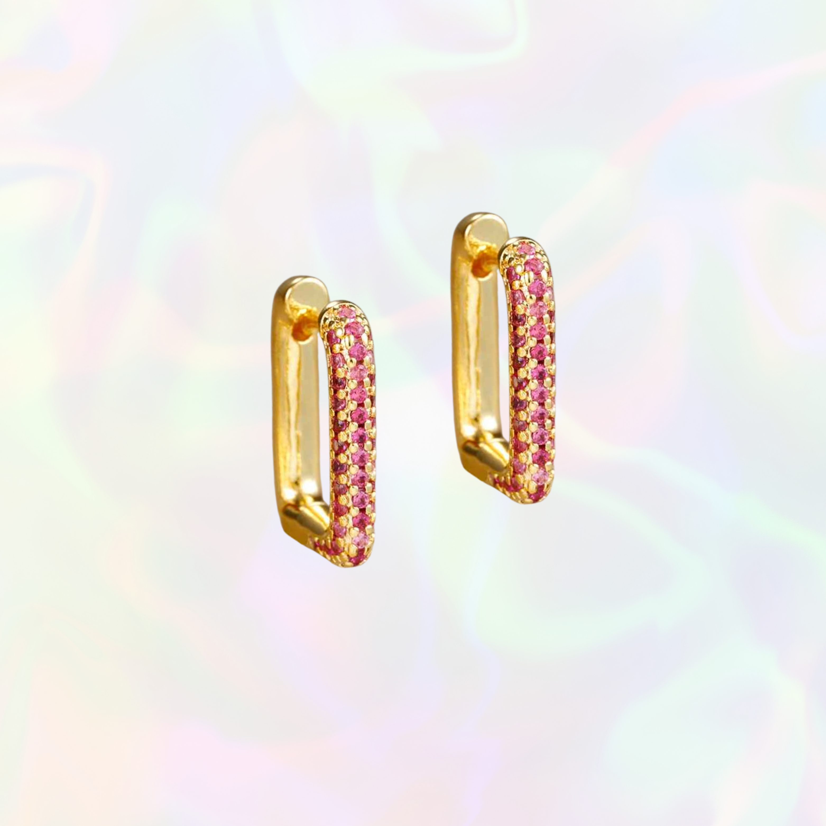 Gold rectangular hoop earrings with pink gemstones on a rainbow gradient background
