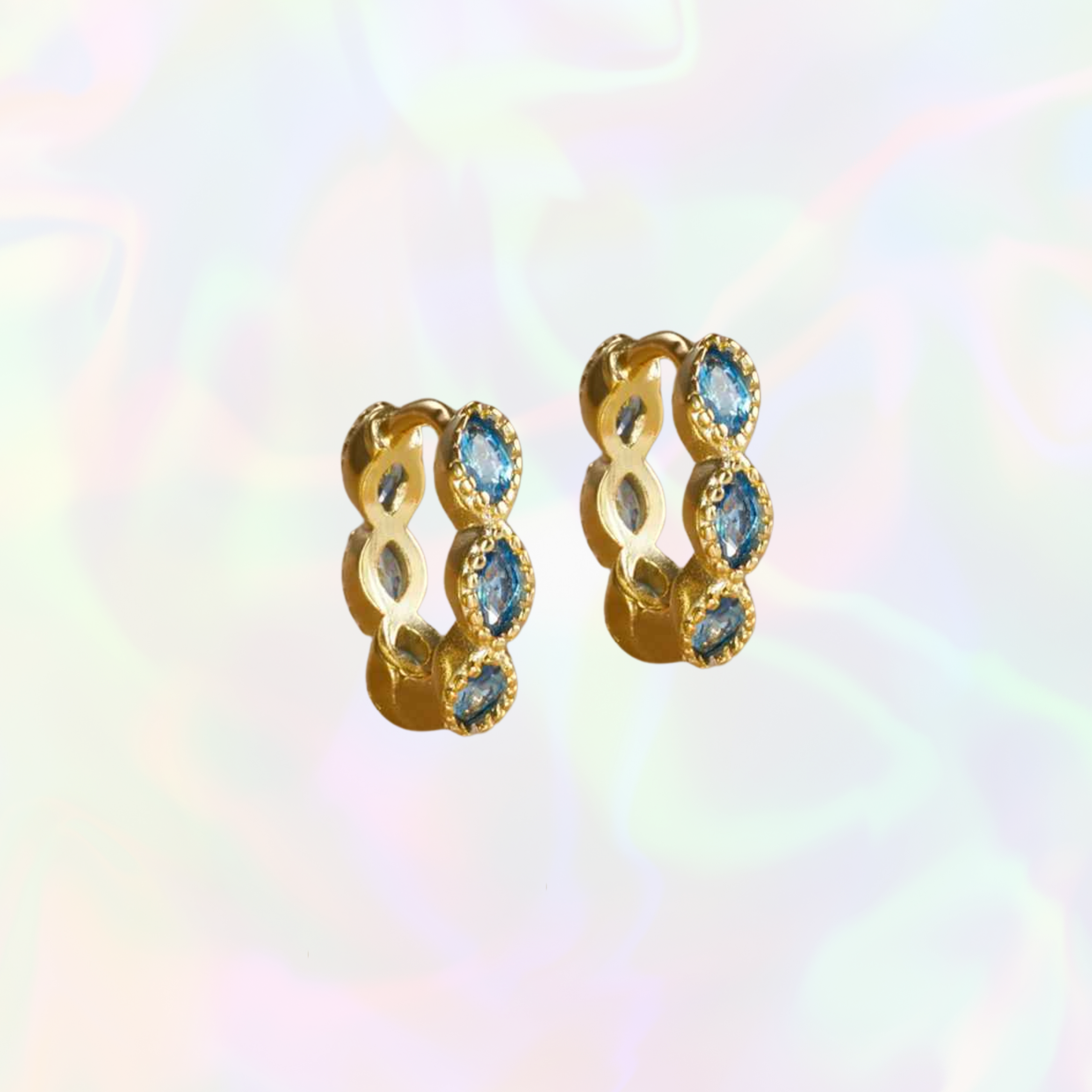 Gold hoop earrings with blue gemstones on a multicolored background