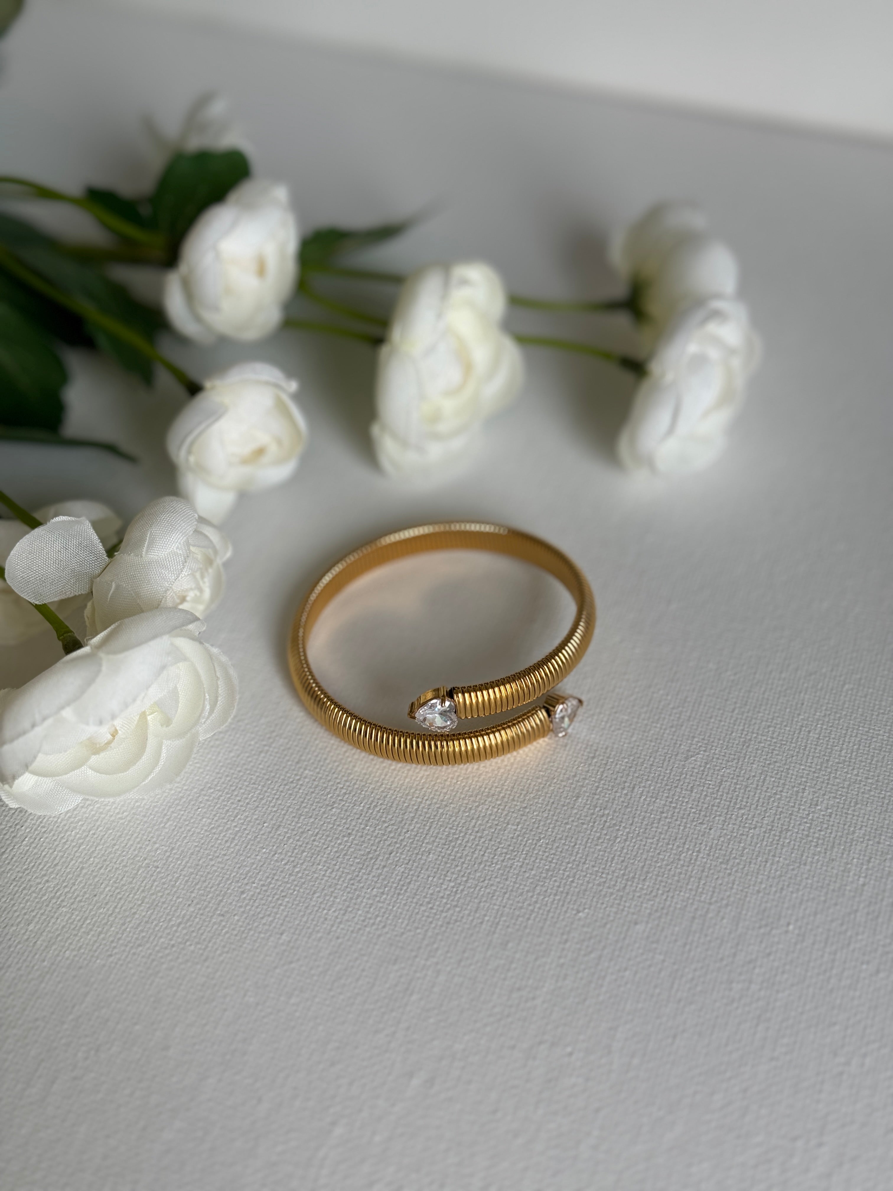 Gold stainless steel bracelet with small diamonds on a light gray surface with white flowers.