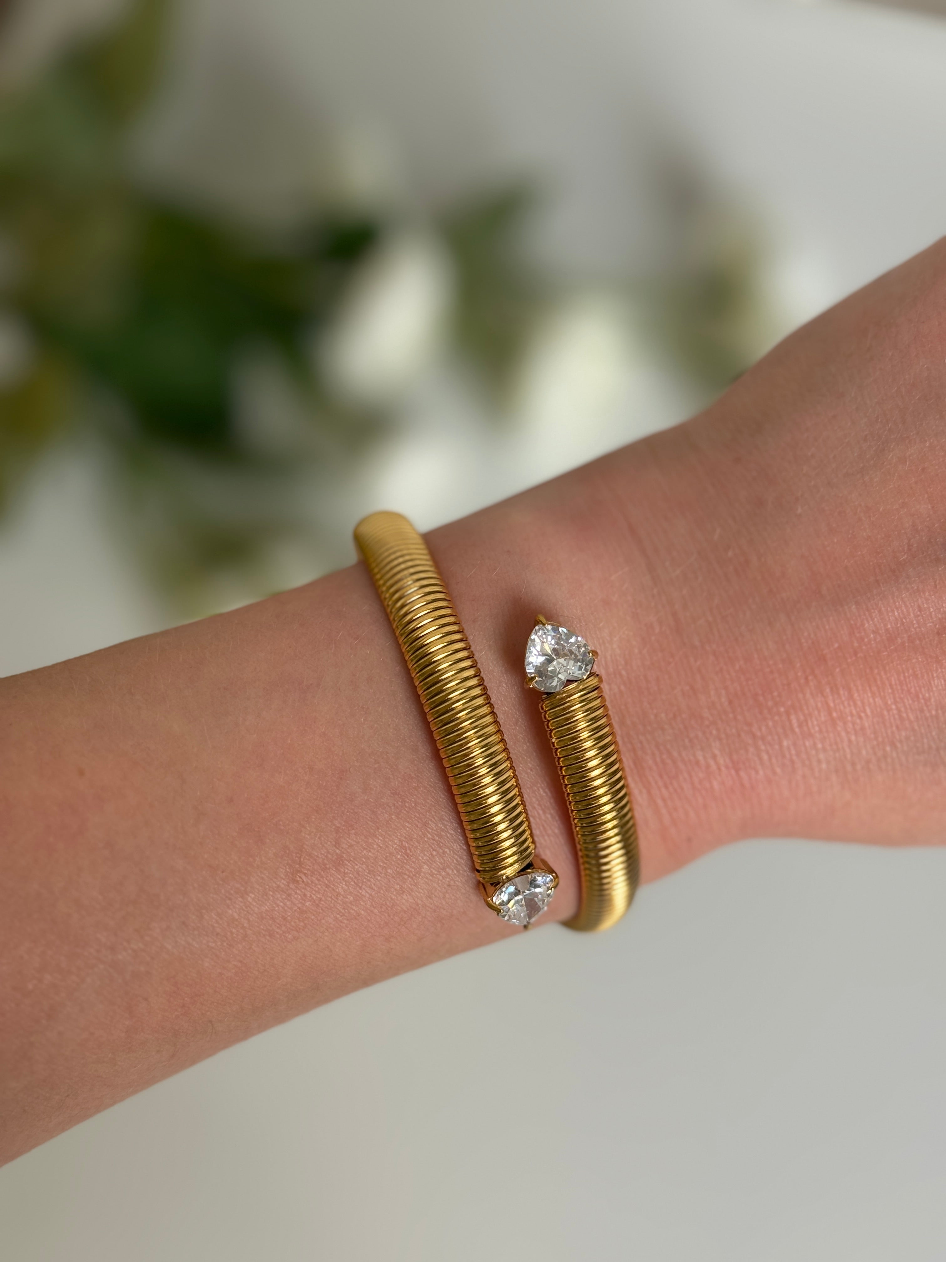 Gold waterproof bracelet with heart shaped gemstone accents on a wrist against a blurred natural background