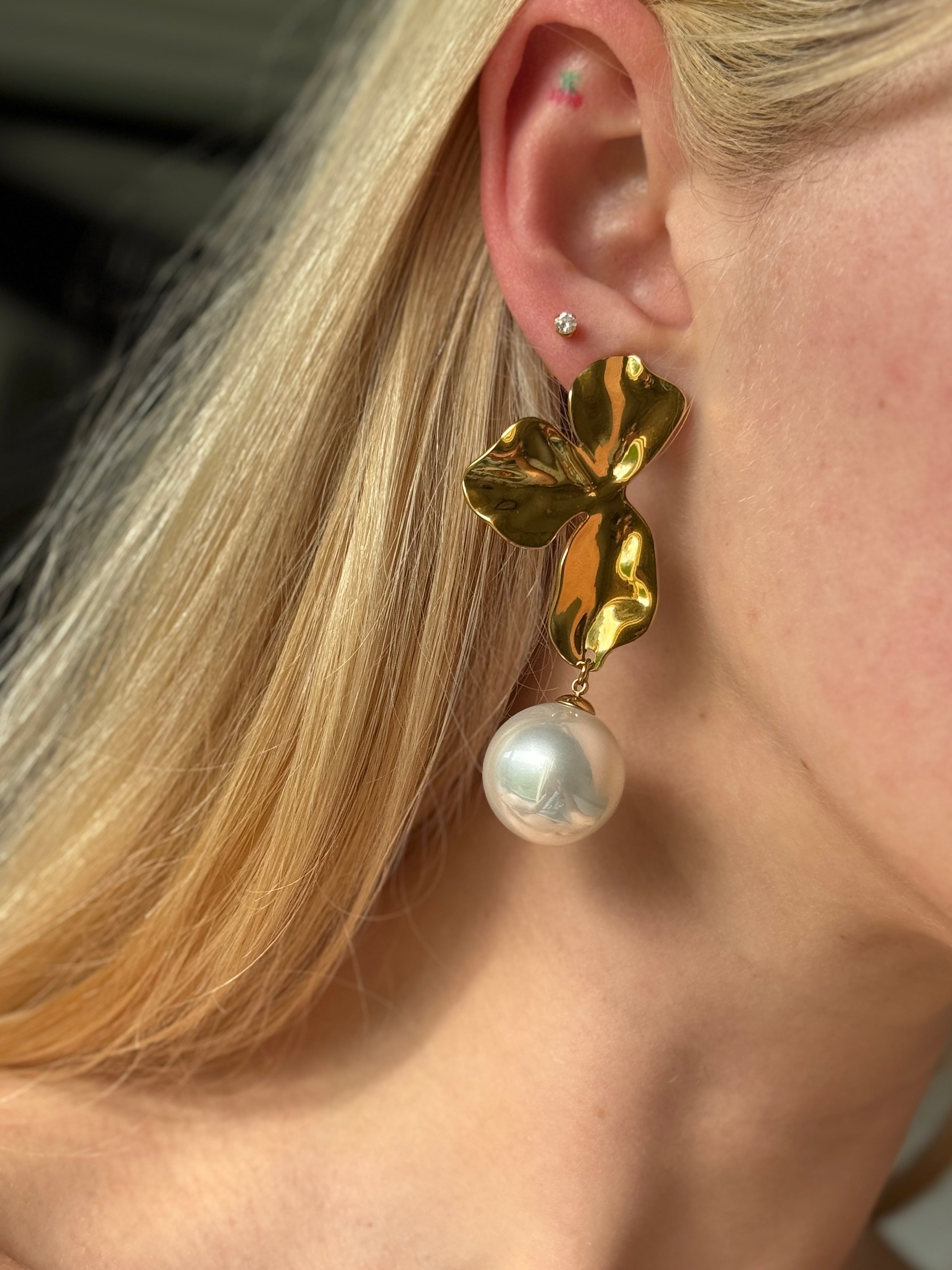 Gold waterproof earring with a pearl drop worn by a person with blonde hair.
