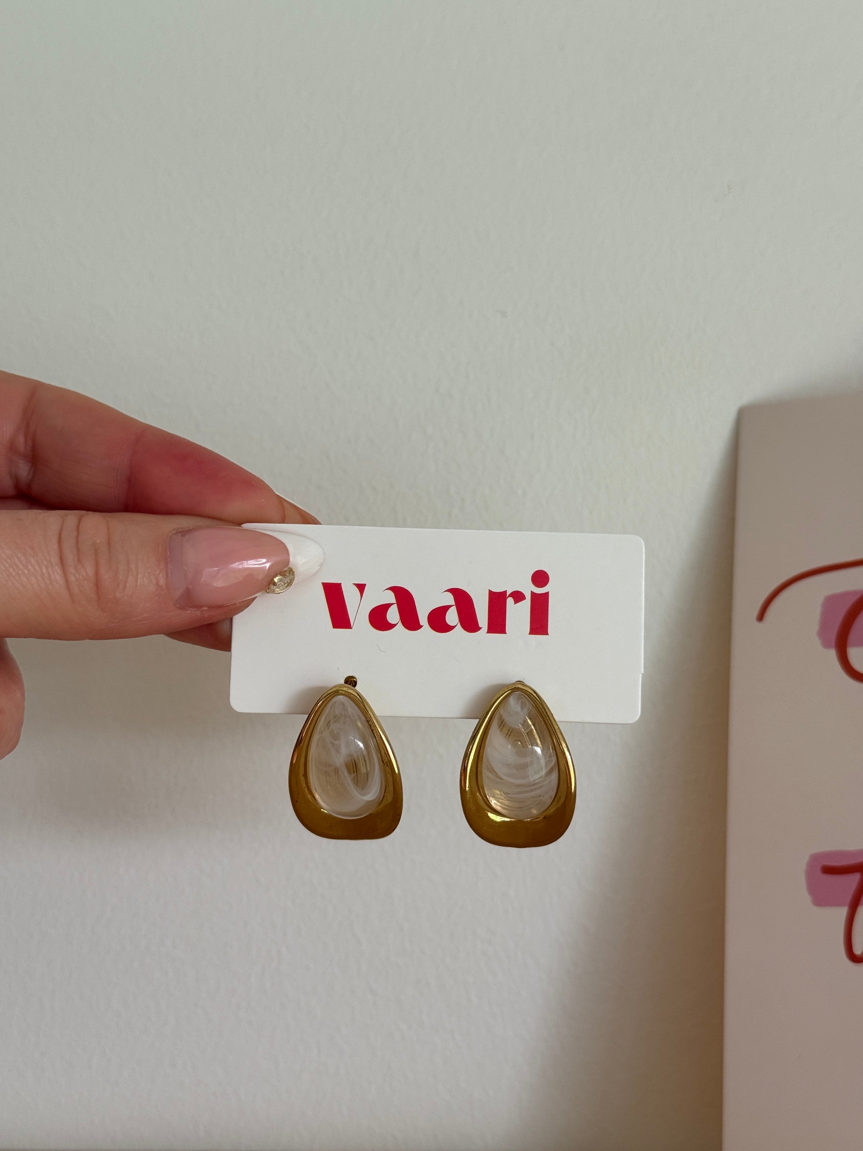Gold teardrop earrings on a 'Vaari' branded card held by a hand against a light background.