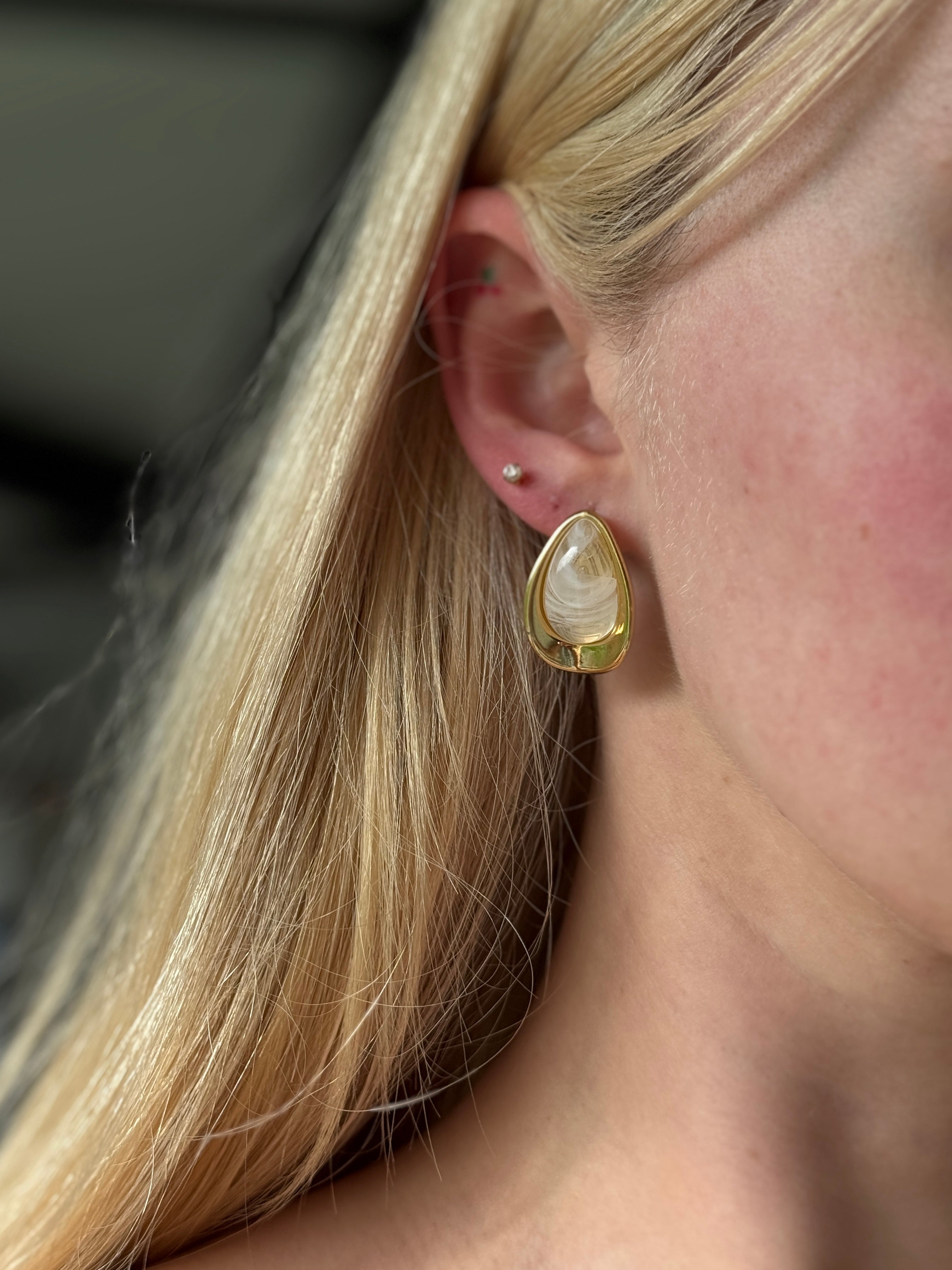 Close-up of a person wearing a gold stainless steel earring with a clear gemstone.