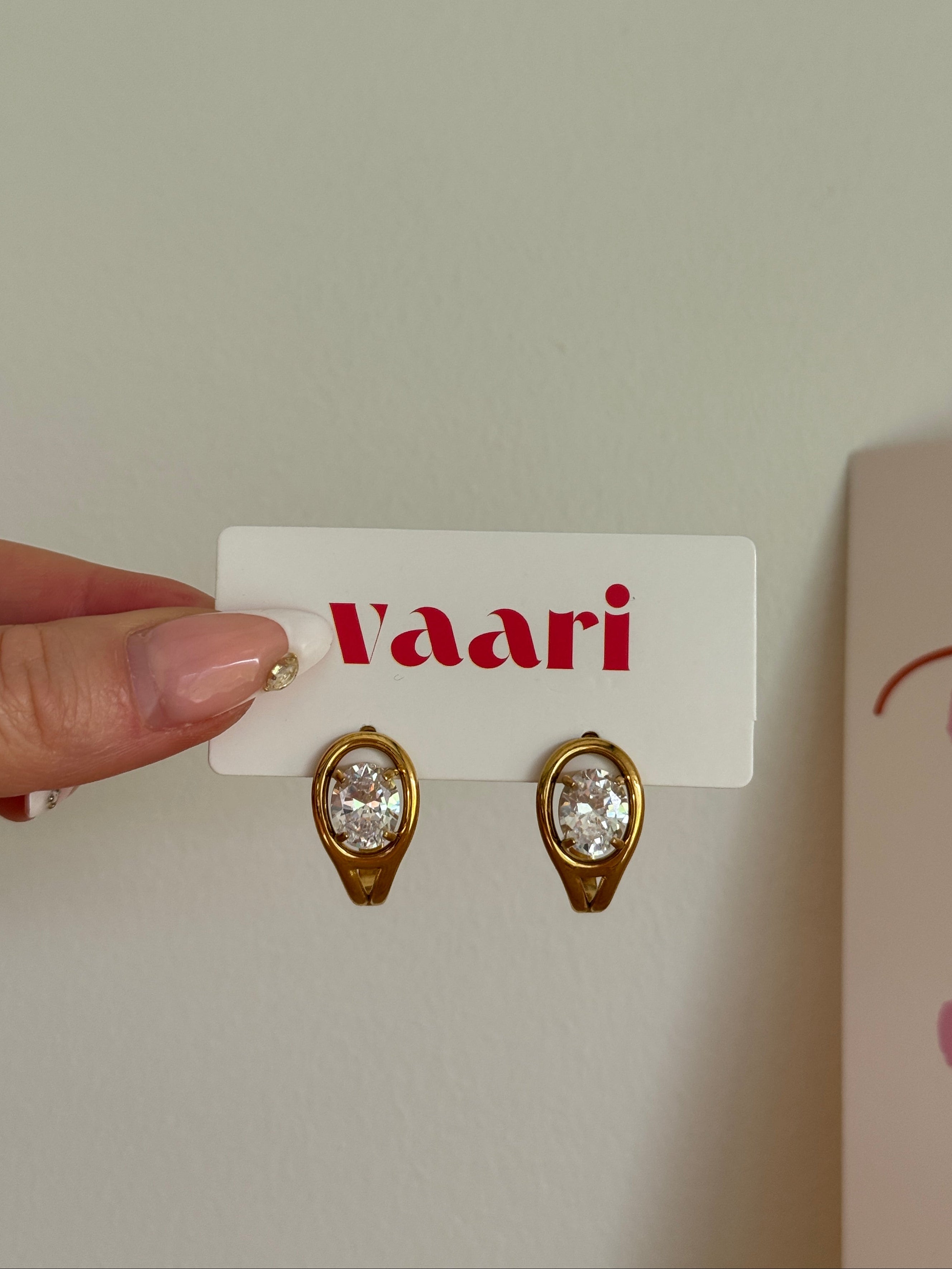 Gold gemstones earrings on a 'Vaari' branded card held by a hand against a neutral background