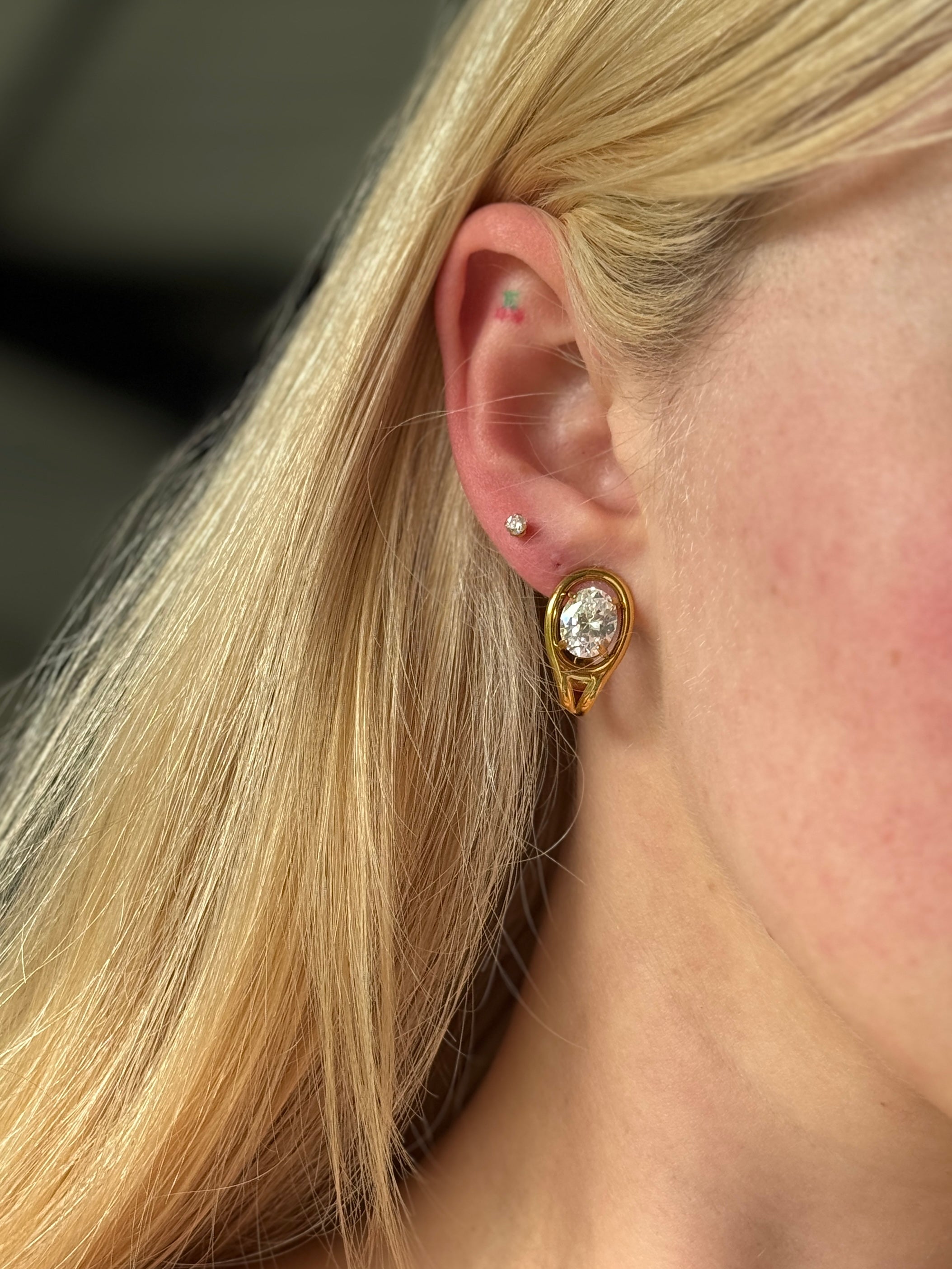 Close-up of a person wearing a gold stainless steel earring with a big clear gemstone.
