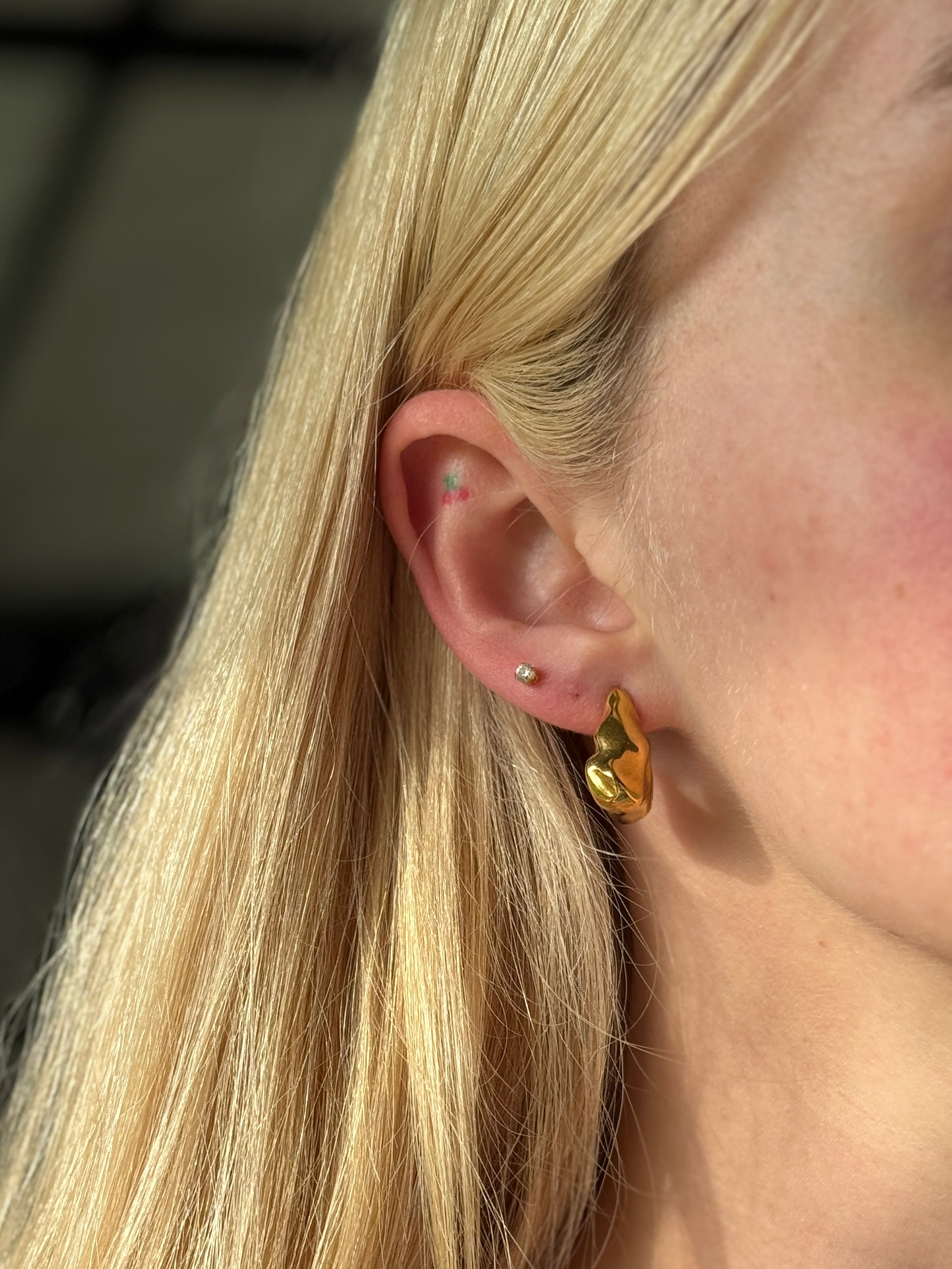 Close-up of a person wearing stainless steel gold hoop earrings with a blurred background